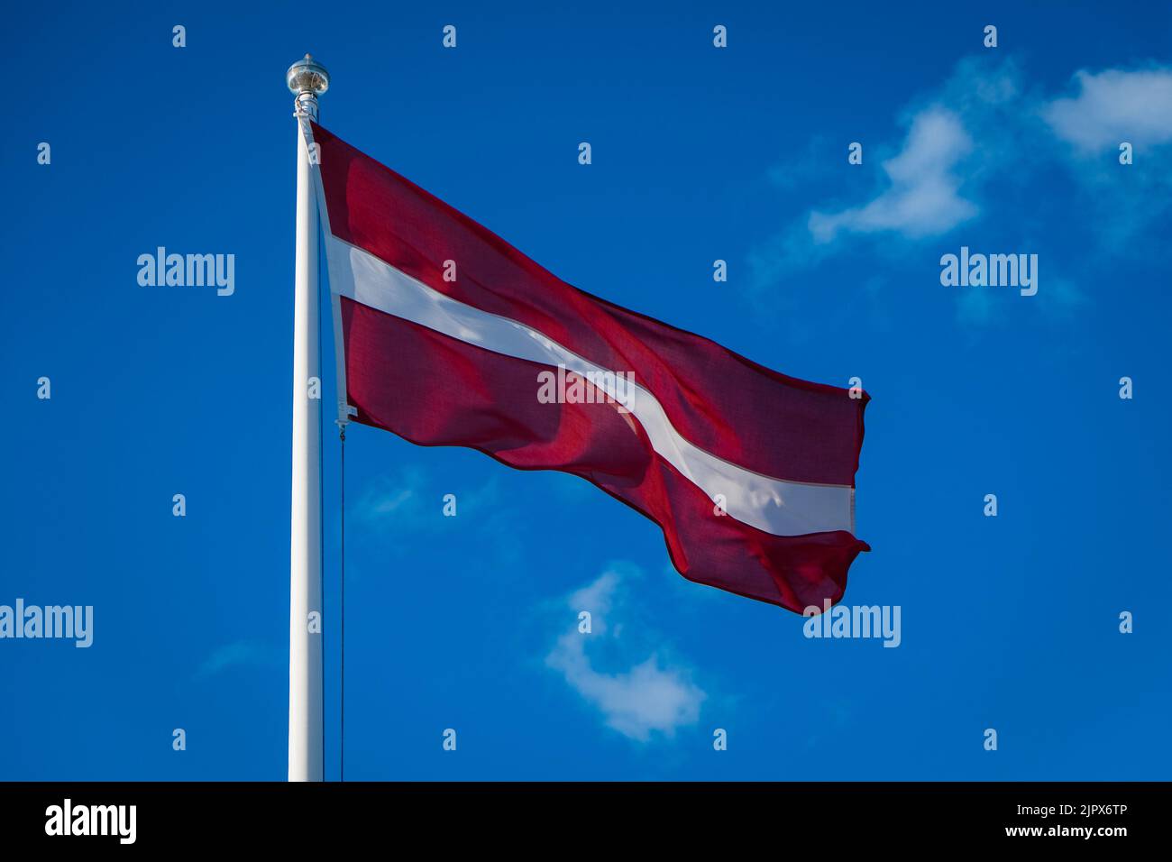 Die lettische Flagge winkt im Wind. Flagge Lettlands auf blauem Himmel Hintergrund. Stockfoto