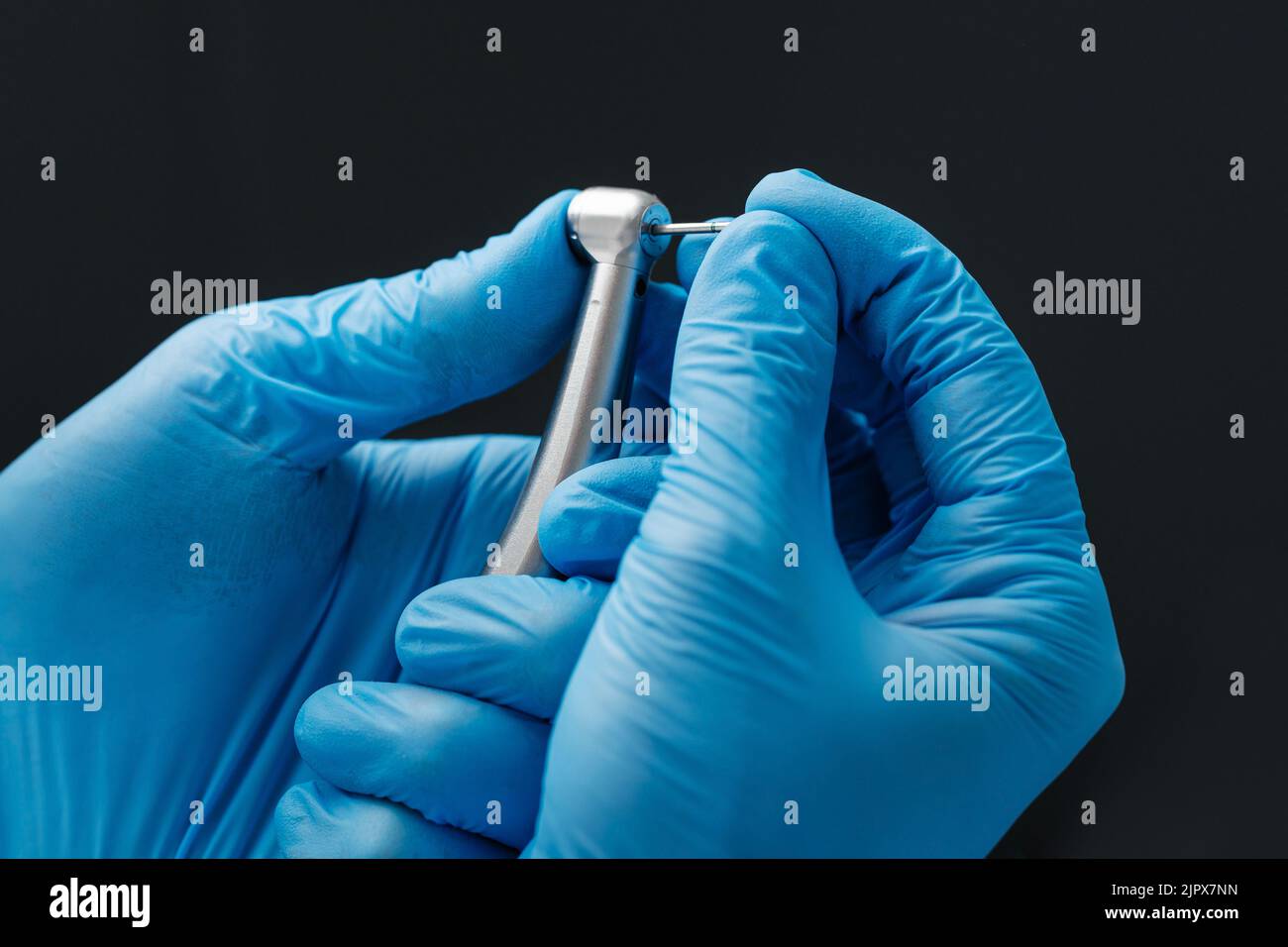 Ein Foto aus der Nähe einer Hand eines Zahnarztes, der eine zahnärztliche Hochgeschwindigkeits-Turbine in das Edelstahlhandstück der Turbine hält. Stockfoto