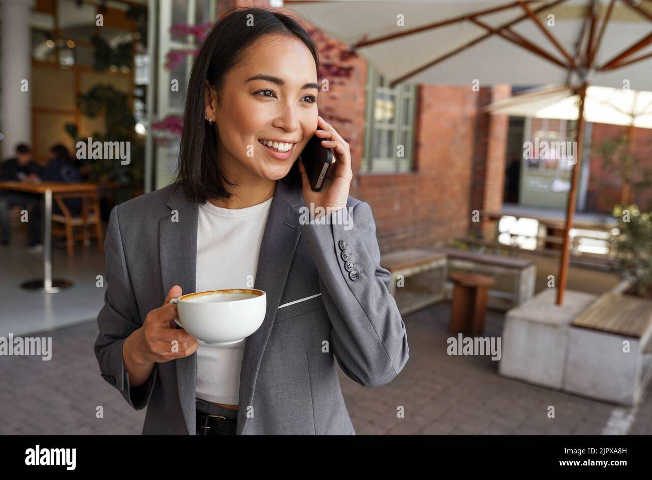 Lächelnde asiatische professionelle Frau, die vor dem Büro auf dem Handy spricht. Stockfoto