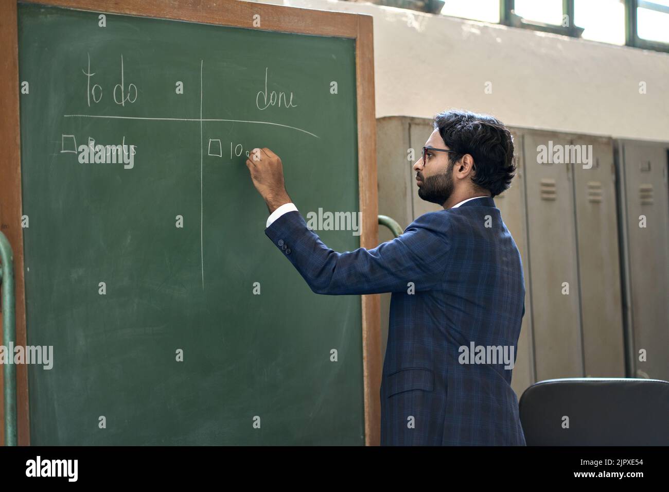 Vielbeschäftigter indischer Geschäftsmann, der im Büro arbeitet und einen Projektplan an der Tafel schreibt. Stockfoto
