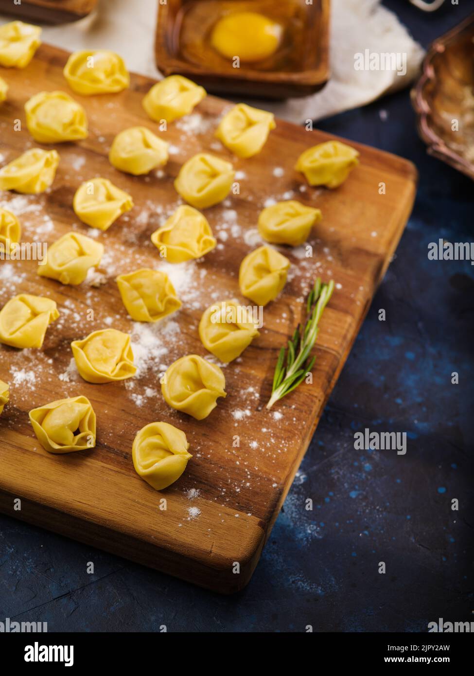 Hausgemachte Knödel auf einem Schneidebrett mit einem Zweig Rosmarin auf einem dunkelblauen Hintergrund warten darauf, gekocht zu werden. Köstliche hausgemachte Fleischrezepte. Stockfoto