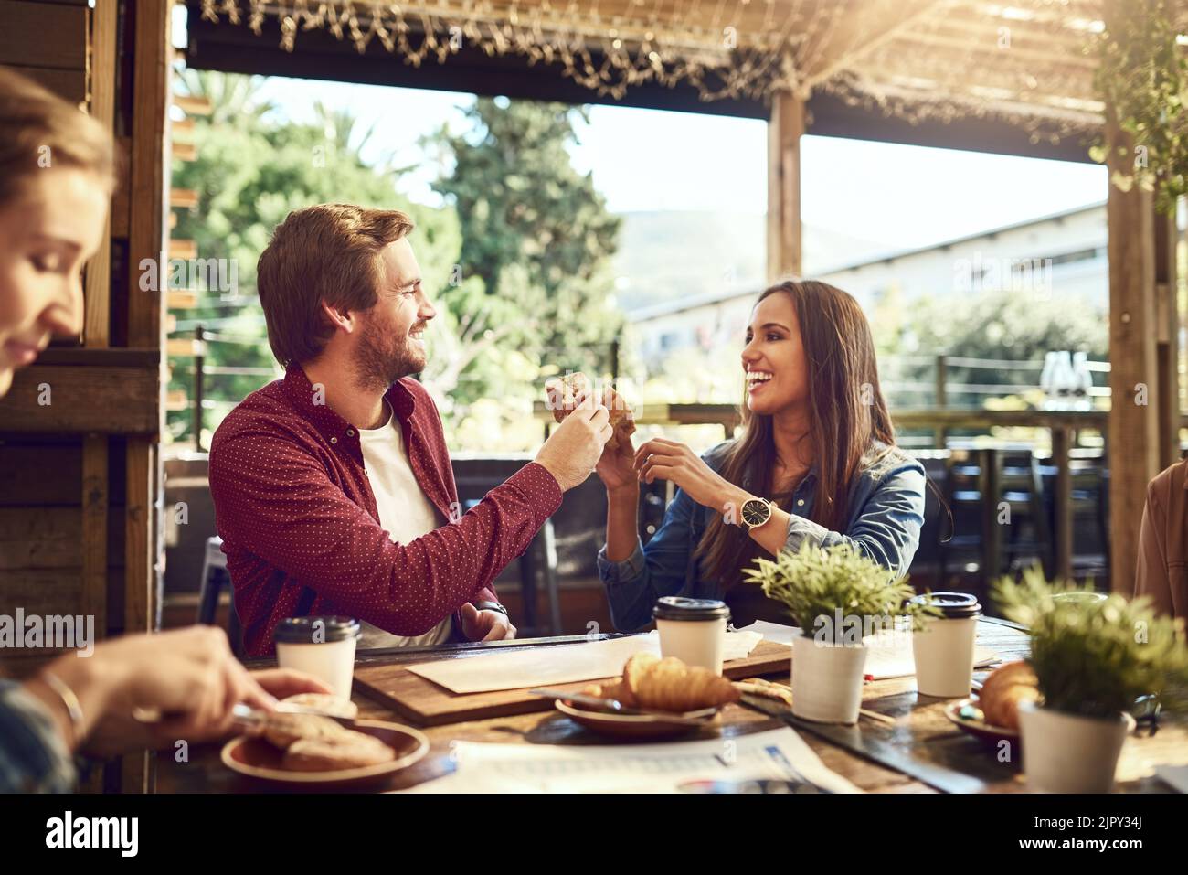 Jubel zu gutem Essen und gut aussehenden Menschen. Ein liebevolles junges Paar toasting mit Sandwiches, während sie sich beim Mittagessen genießen. Stockfoto
