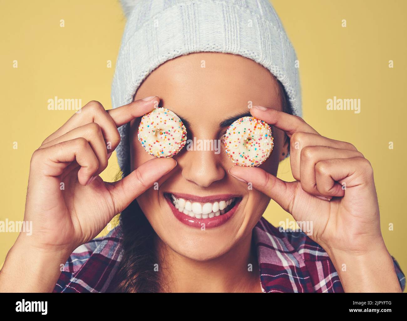 Keine Augenweide, keine Seelennahrung. Eine junge Frau bedeckt ihre Augen mit Keksen vor einem bunten Hintergrund. Stockfoto