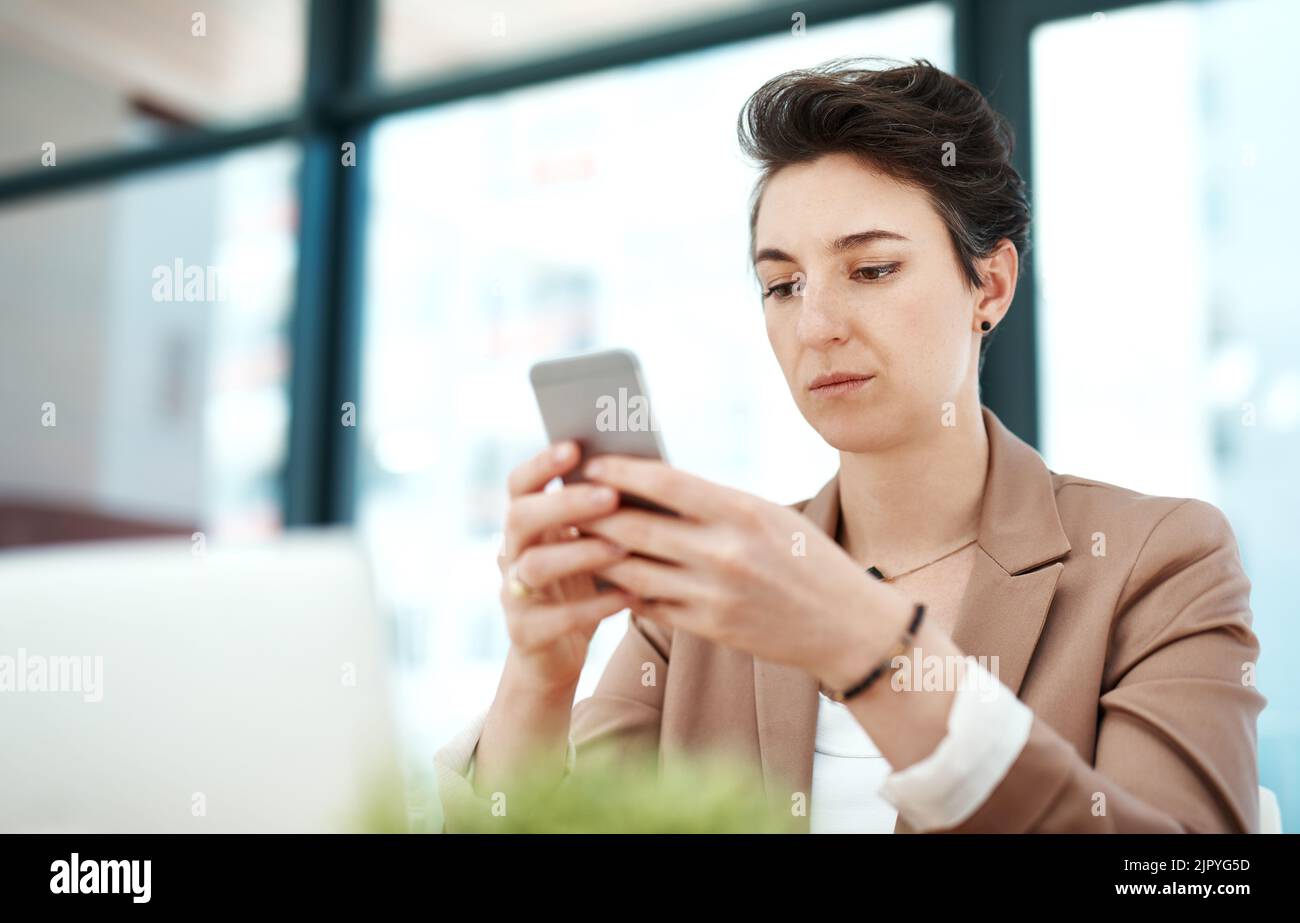 Ich sollte meine Meetings absagen... eine junge Designerin, die ihr Telefon an ihrem Schreibtisch benutzt. Stockfoto