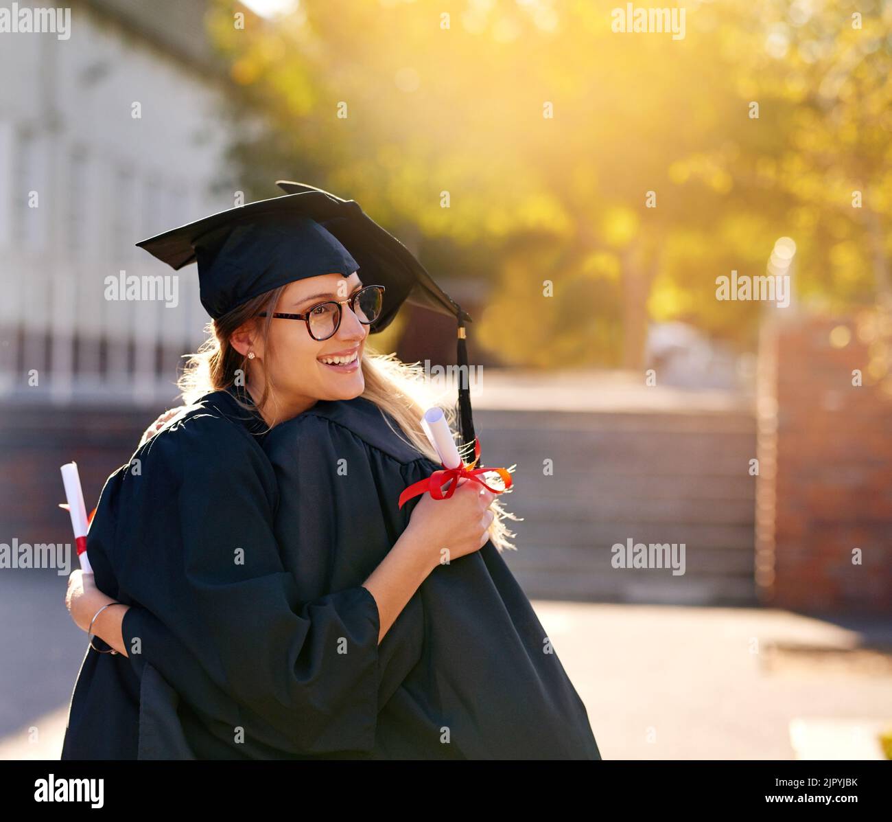 Ich bin so stolz darauf, wie weit wir gekommen sind. Zwei Studenten umarmen sich am Abschlusstag. Stockfoto