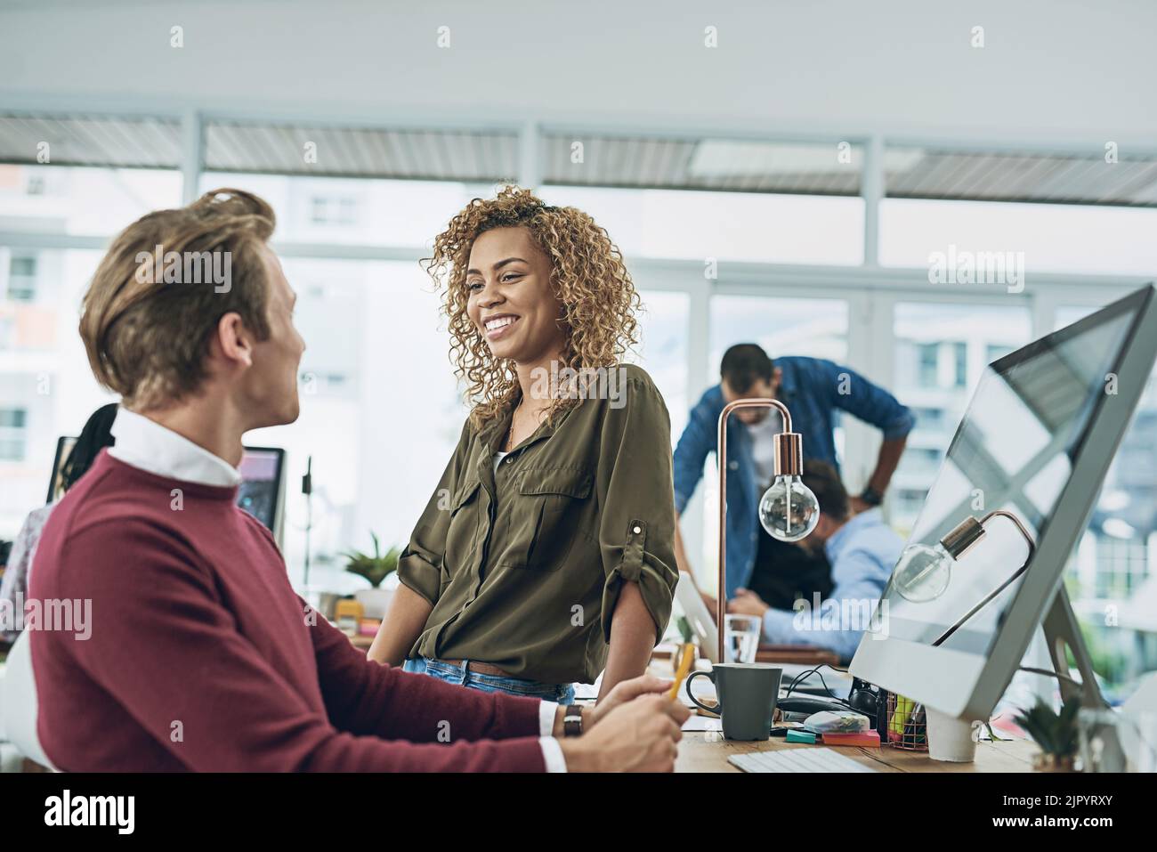 Eine offene Arbeitsumgebung sorgt für offene und freundliche Gespräche. Zwei junge Kollegen unterhalten sich in einem modernen Büro freundlich. Stockfoto
