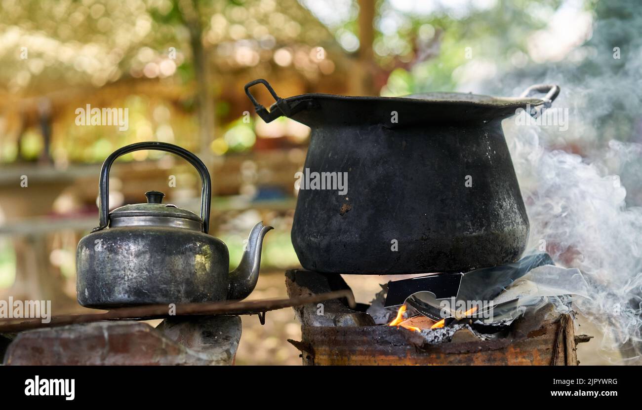 Ein großer schwarzer Topf und ein alter Wasserkocher auf einem Feuer im Freien. Stockfoto