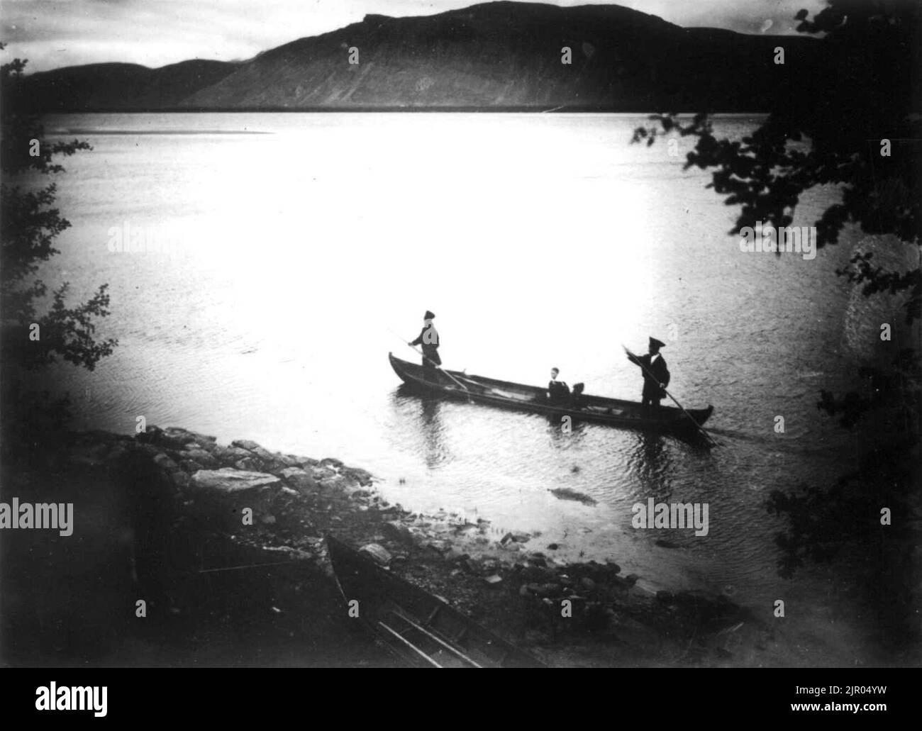 To personer staker seg frem i elvebåt, forbi Langnes, Tana, Finnmark, antatt 1900-10 Stockfoto