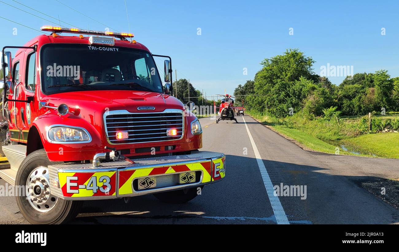 Ein roter Feuerwehrwagen mit einem Rettungshubschrauber dahinter auf einer von Grünflächen umgebenen Straße Stockfoto