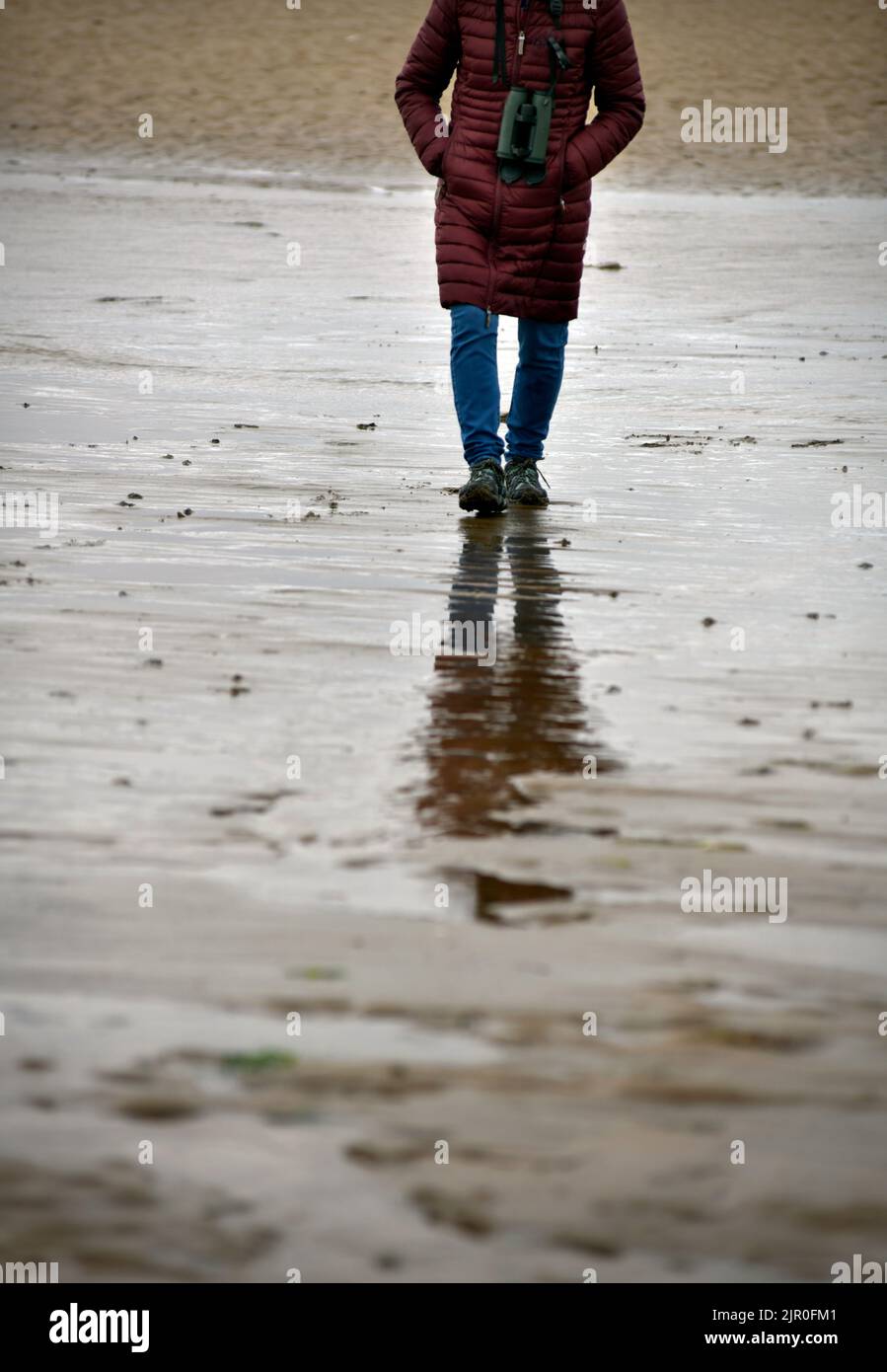 Eine alleinreisende Frau, die am nassen Strand von holme im Norden von norfolk england spazierengeht Stockfoto