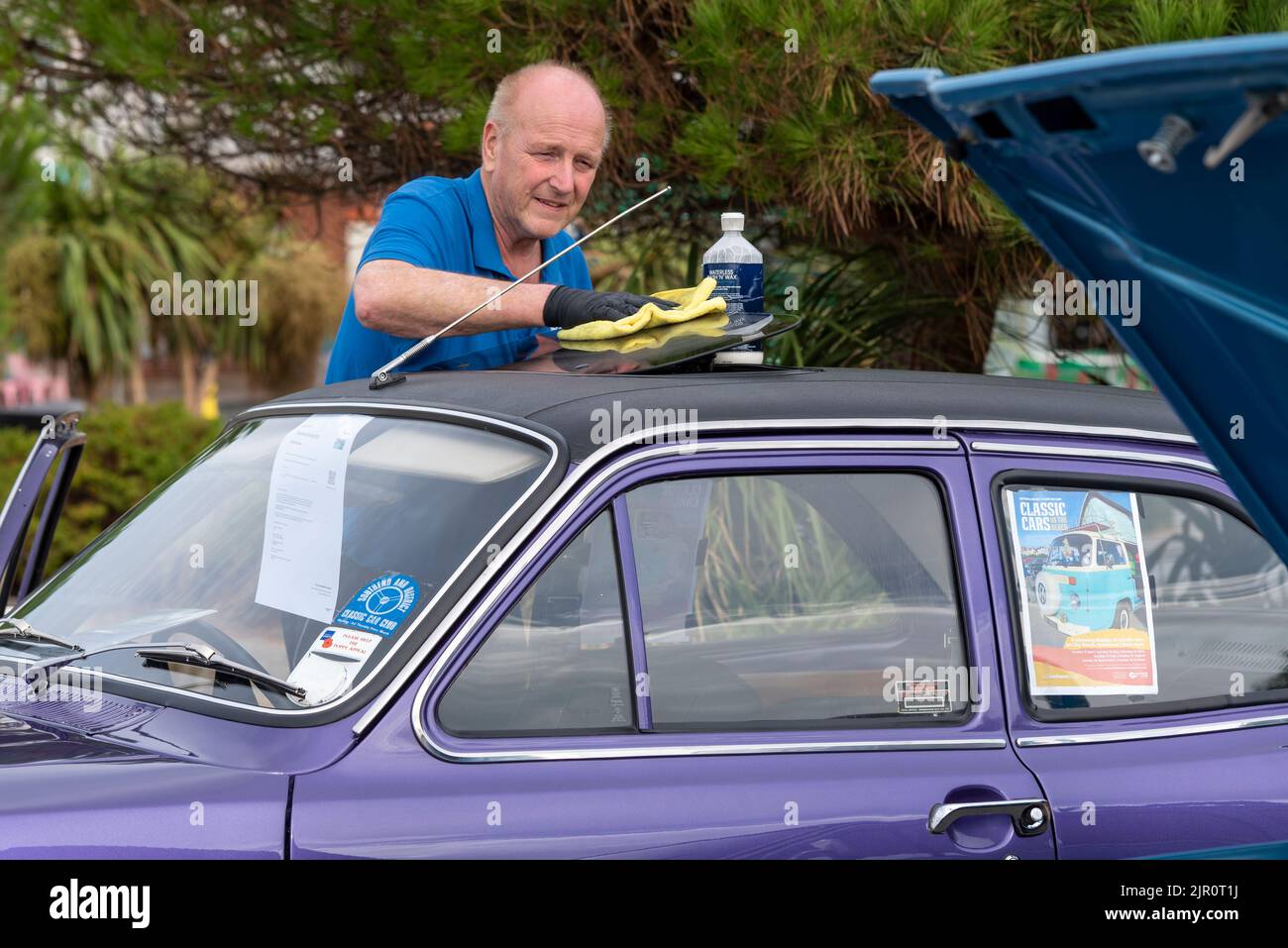 Southend on Sea, Essex, Großbritannien. 21. August 2022. Das heiße Wetter in der neuen Stadt Southend on Sea setzt sich fort, viele Menschen sind bereits früh am Morgen draußen, da die bewölkten frühen Wolken sich klären. Die Leute genießen die Promenadenautoshow. Ein Mann, der einen Ford Escort MkI poliert Stockfoto
