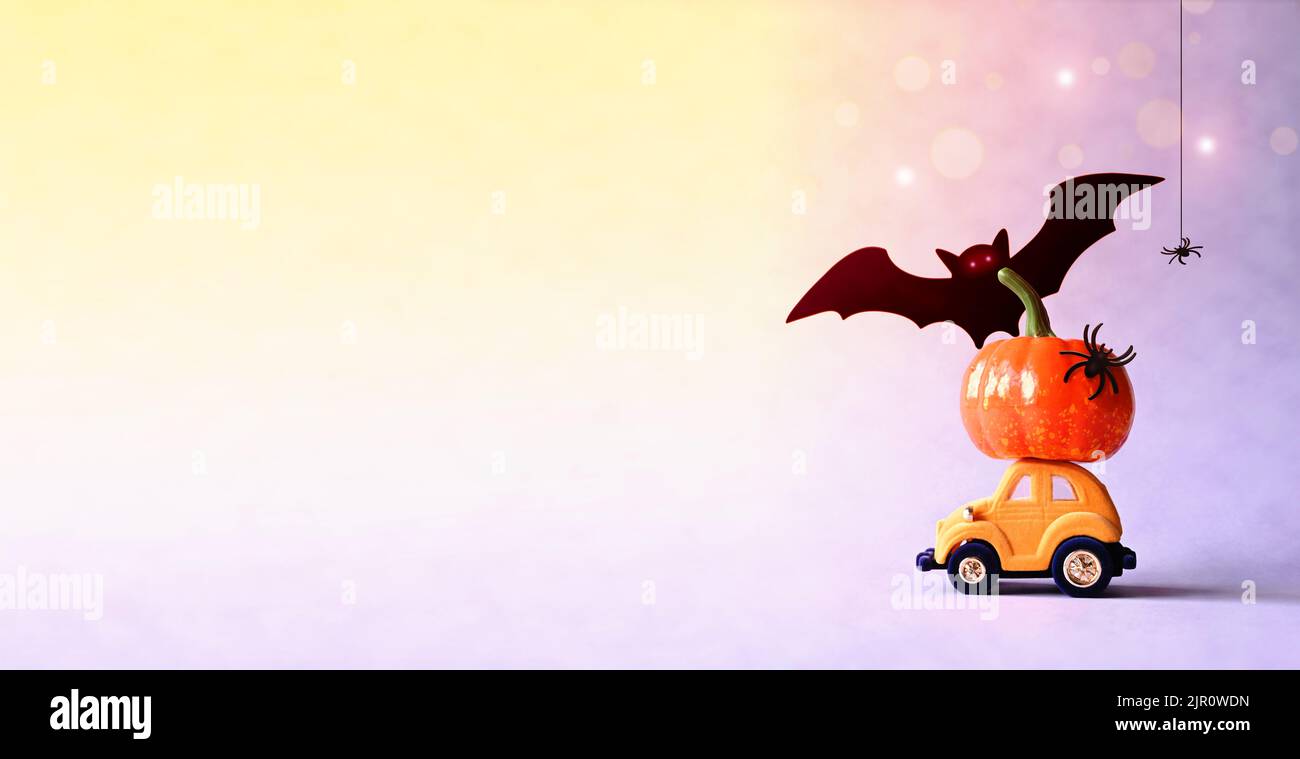 Spielzeugauto mit witzigem Kürbis auf dem Dach und Fledermäusen auf violettem Hintergrund. Platz für Text. Halloween Hintergrund. Stockfoto