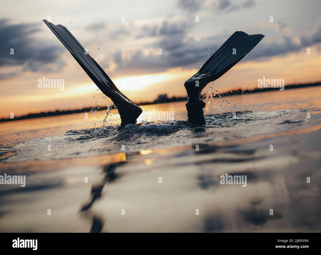 Taucher, die mit seinen Flossen über dem Wasser ins Meer tauchen. Mann beim Tauchen bei Sonnenuntergang. Stockfoto
