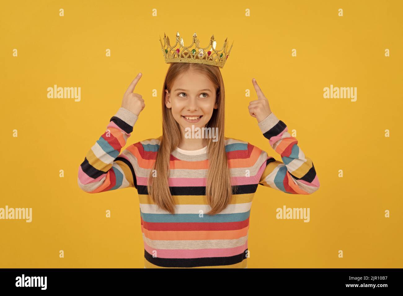 Happy teen Kind zeigen Finger auf Königin Krone auf gelbem Hintergrund Stockfoto