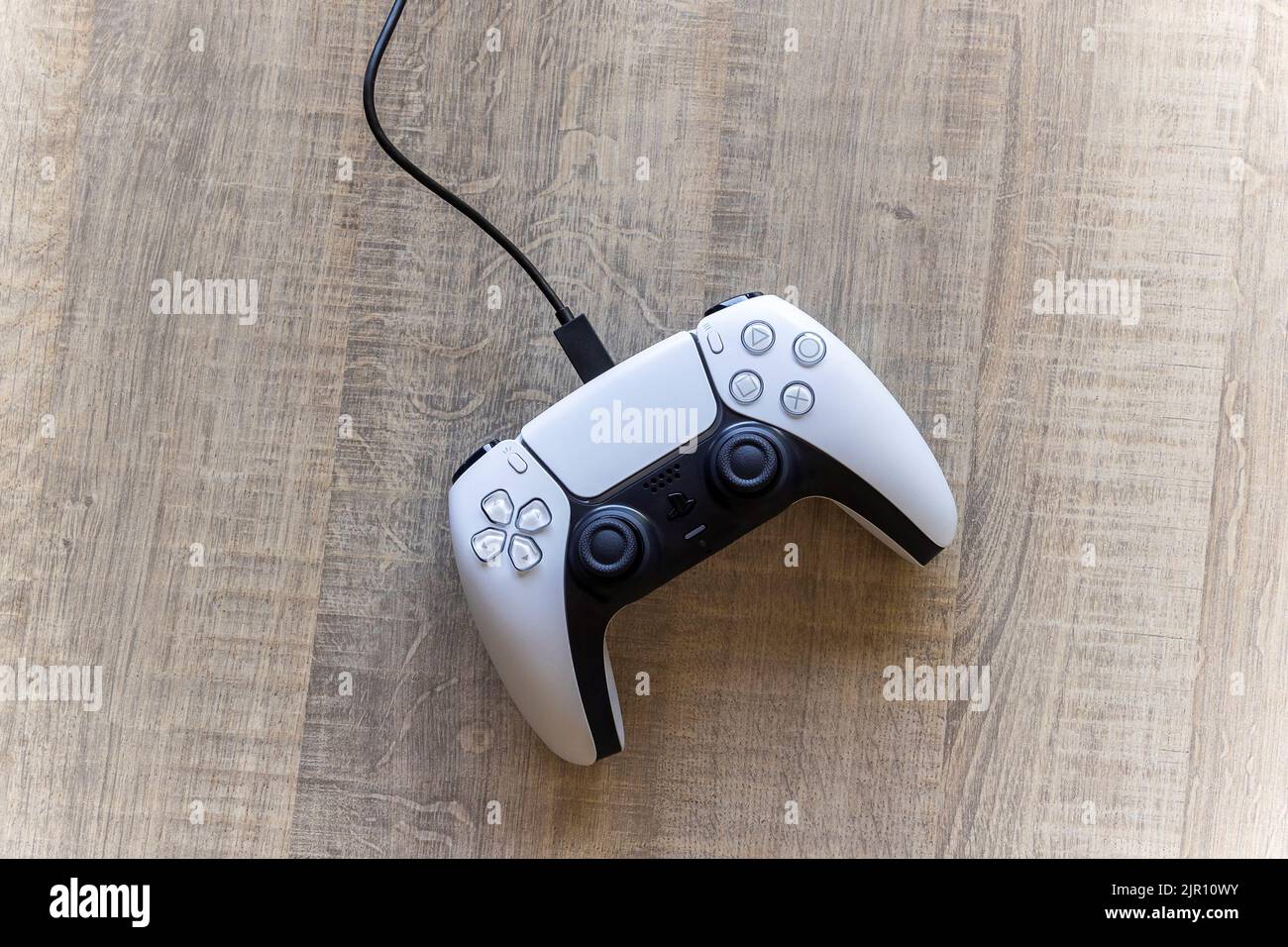 BRECHT, BELGIEN – AUGUST 14 2022: Ein Top-Down-Portrait eines offiziellen weißen Basis-PlayStation 5-Controllers, der mit dem USB-C-Kabel aufgeladen wird. Der Stockfoto