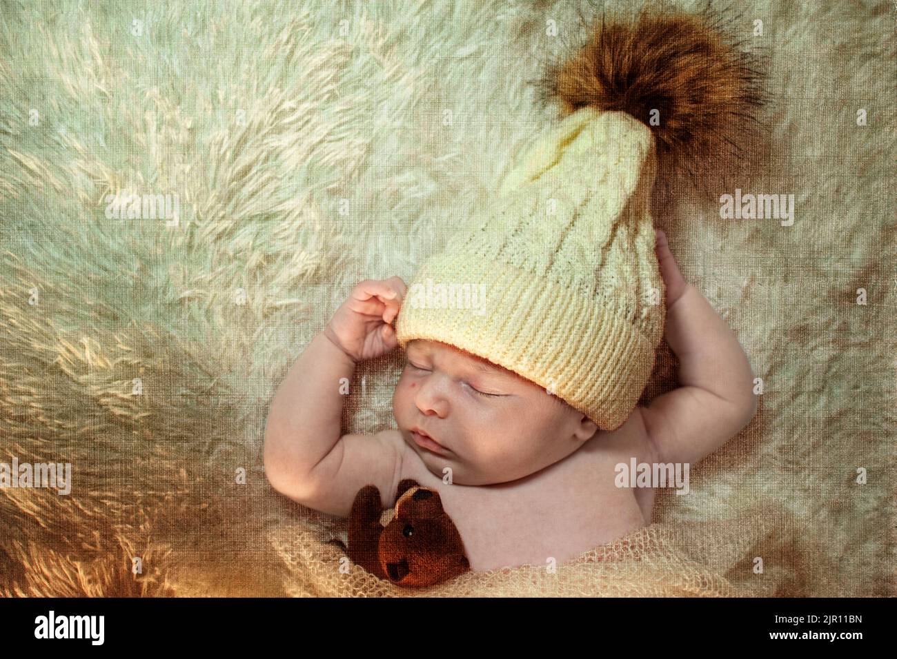 Ästhetisches Bild eines Babys, das mit einem kleinen Teddybären sprittert. Neugeborene trägt eine weiße Wollmütze, die auf einem weißen Teppich spleiert. Künstlerische Bilder für Buchcover Stockfoto