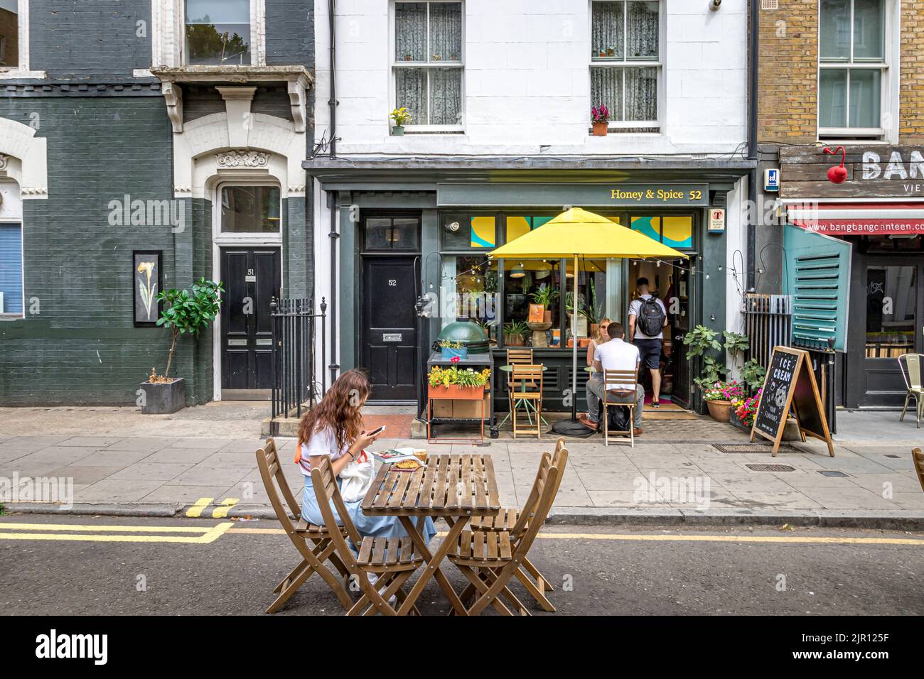 Eine junge Frau, die vor Honey & Spice in der Warren Street, London W1, auf ihr Mobiltelefon schaut Stockfoto