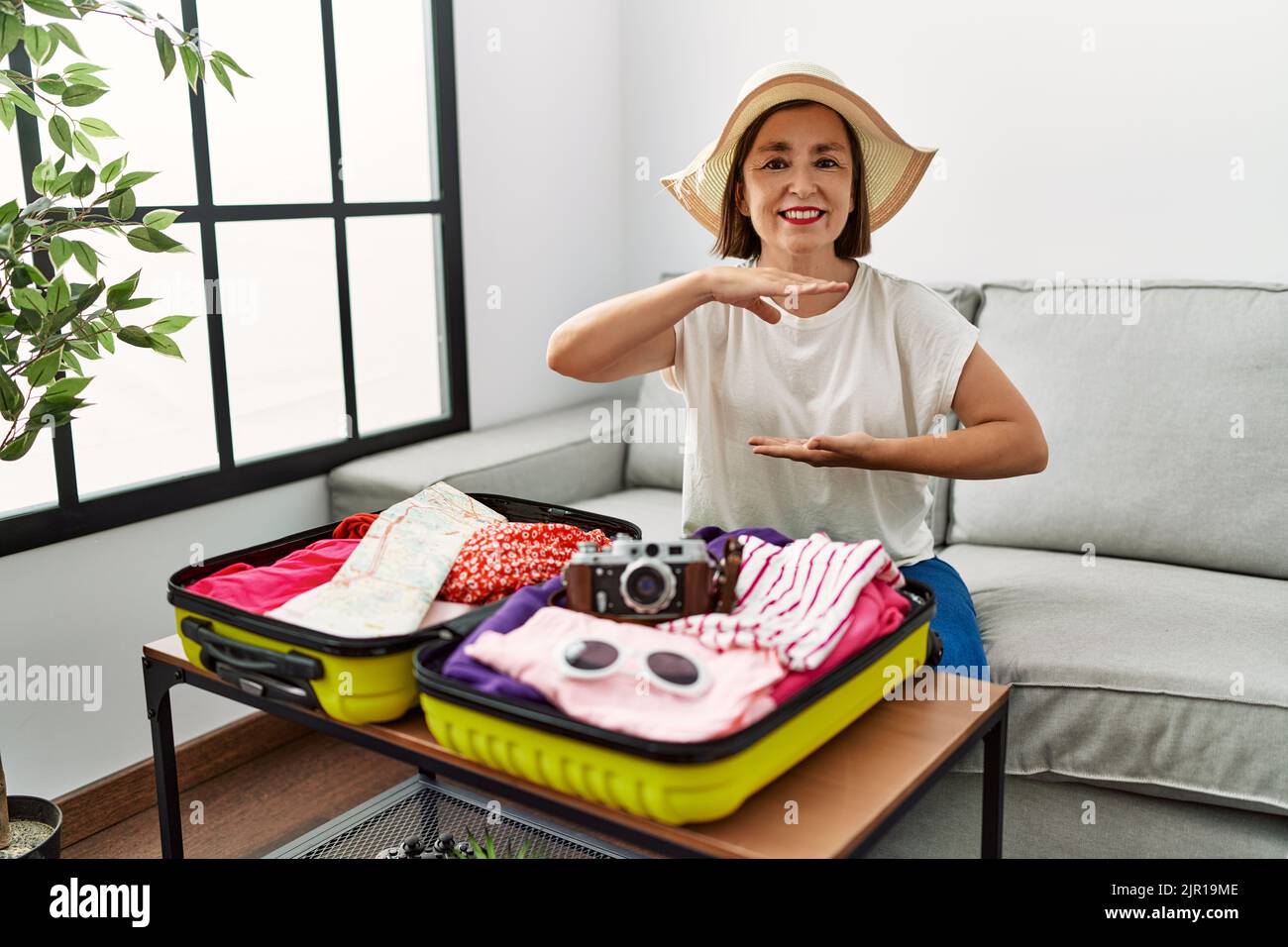 Schöne mittelalterliche hispanische Frau Verpackung Sommerkleidung in Koffer gestikulieren mit Händen zeigen große und große Größe Zeichen, Maßnahme Symbol. Lächelnd l Stockfoto