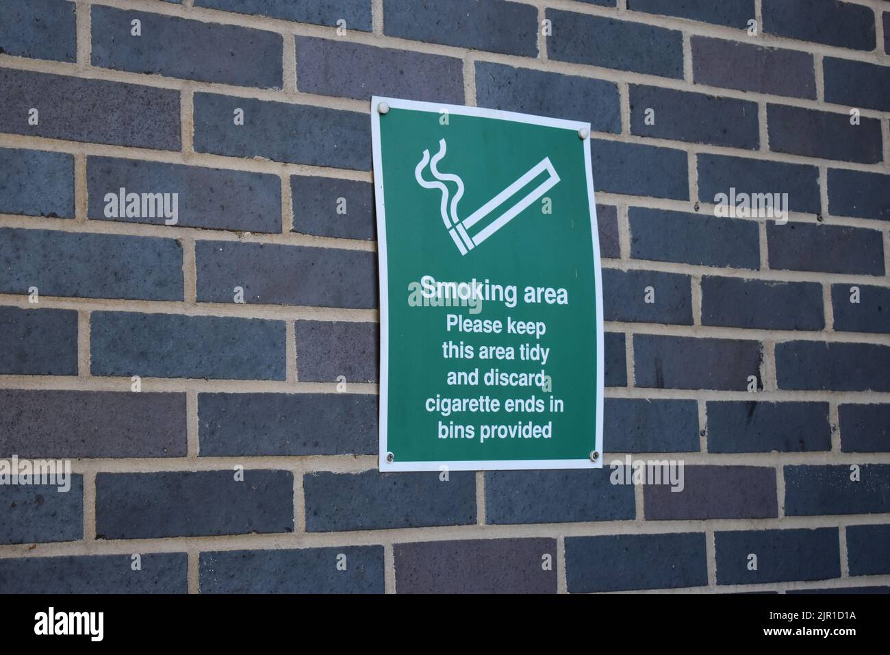 Schild: „Raucherbereich Bitte halten Sie diesen Bereich ordentlich und entsorgen Sie Zigarettenkippen in den bereitgestellten Behältern“ mit Kopierplatz. Stockfoto