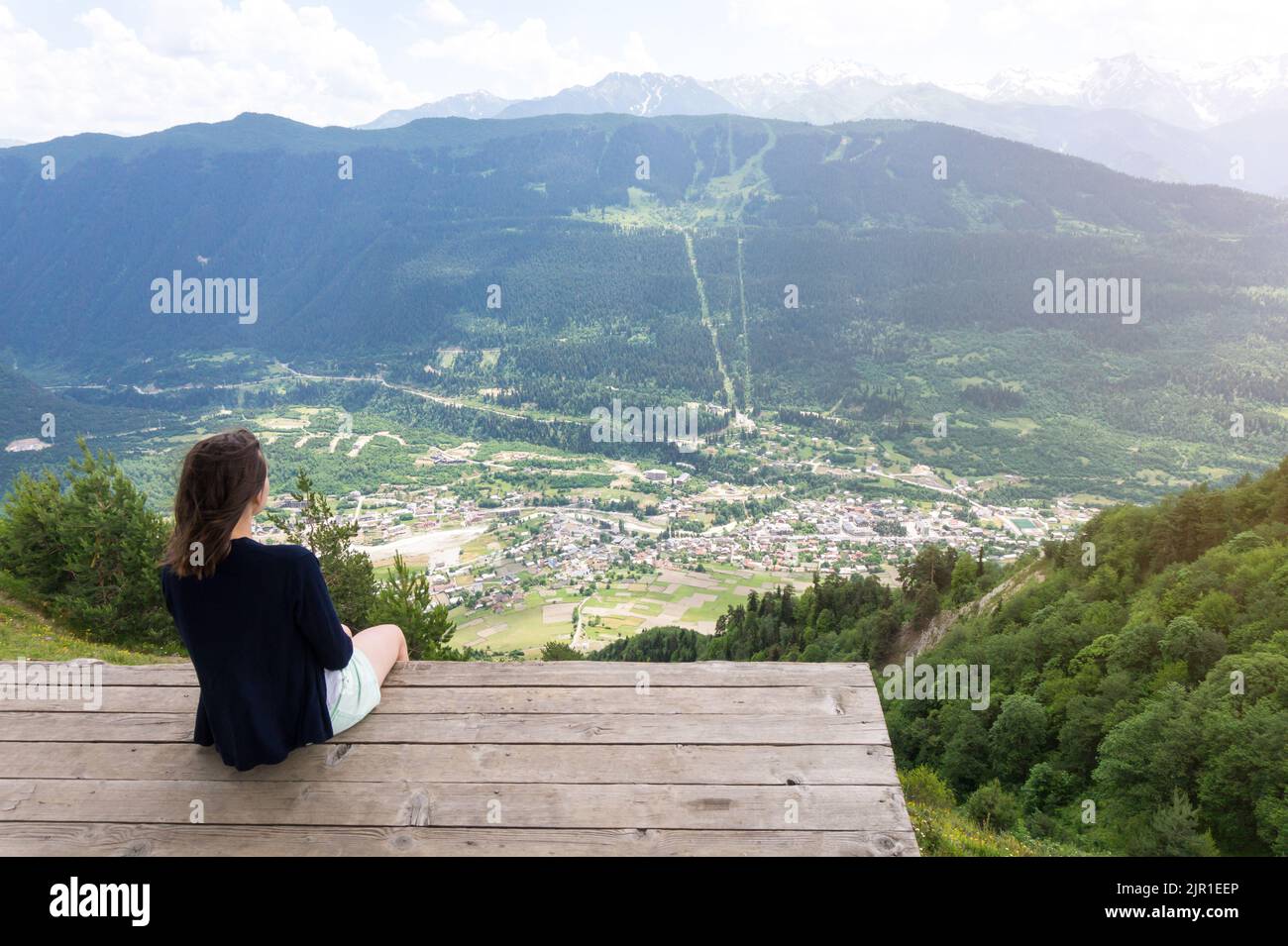 Mestia Dorf Draufsicht vom Aussichtspunkt Cross in der Region Upper Svaneti, Georgien. Unerkennbare junge Frau, die von oben auf Mestia sitzt und sie anschaut Stockfoto