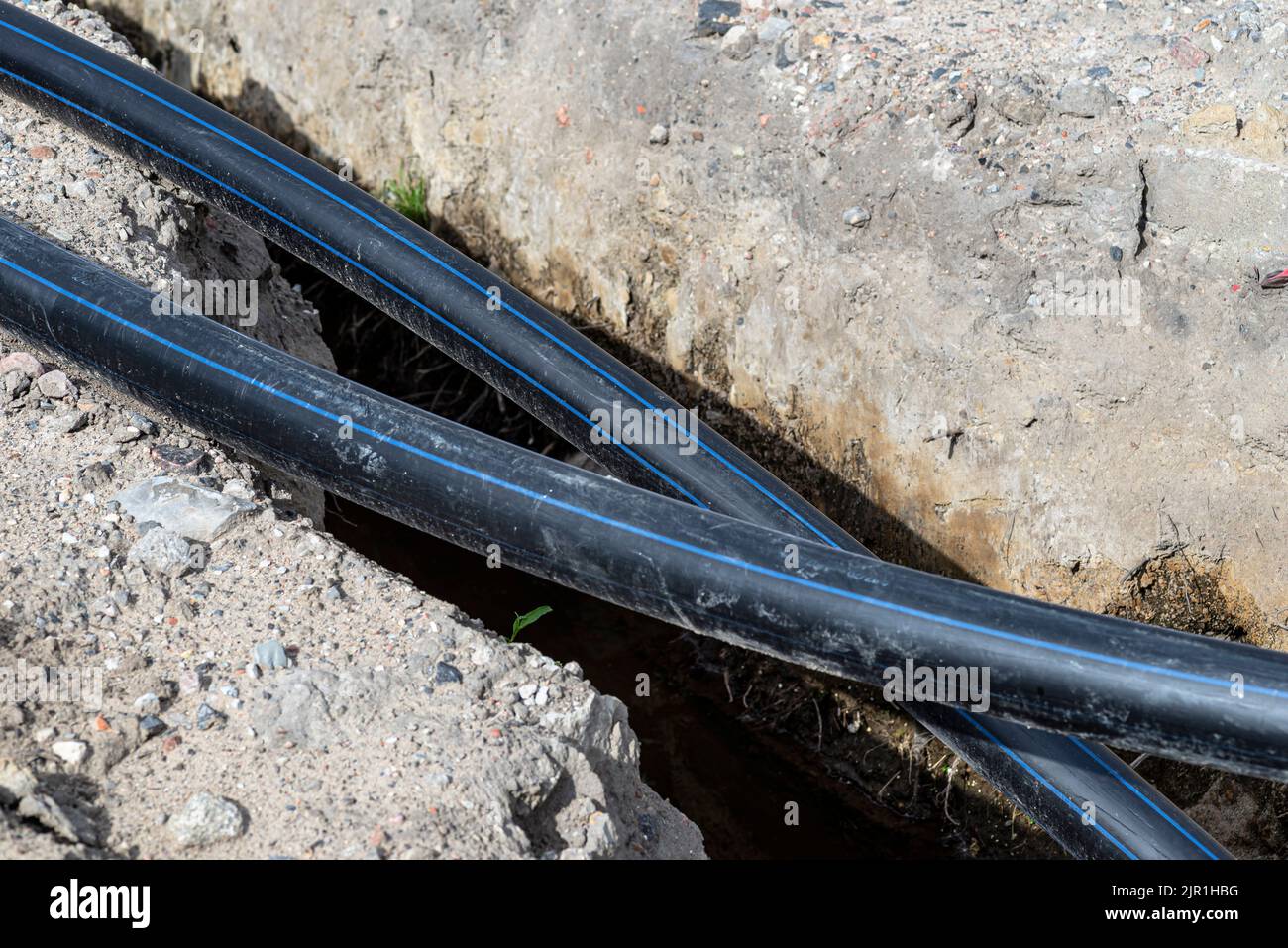 Kunststoff-Wasserleitung entlang des Grabens mit hohem Grundwasser, Wasseranschluss in der Siedlung. Stockfoto