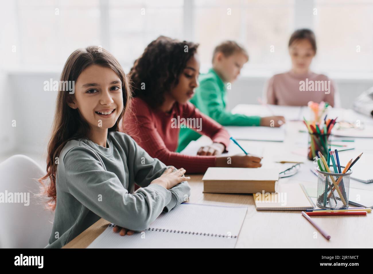 Happy Schoolgirl Sitzt Am Schreibtisch Lächelnd Zur Kamera Im Klassenzimmer Stockfoto