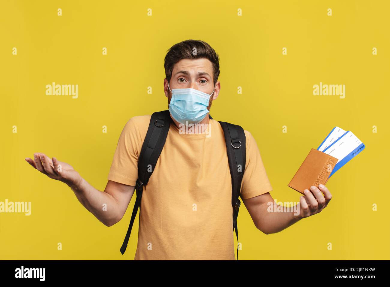 Stornierter Flug. Schockierter männlicher Reisender, der Fahrkarten hält und nach der Stornierung die Hände spricht, gelber Hintergrund Stockfoto
