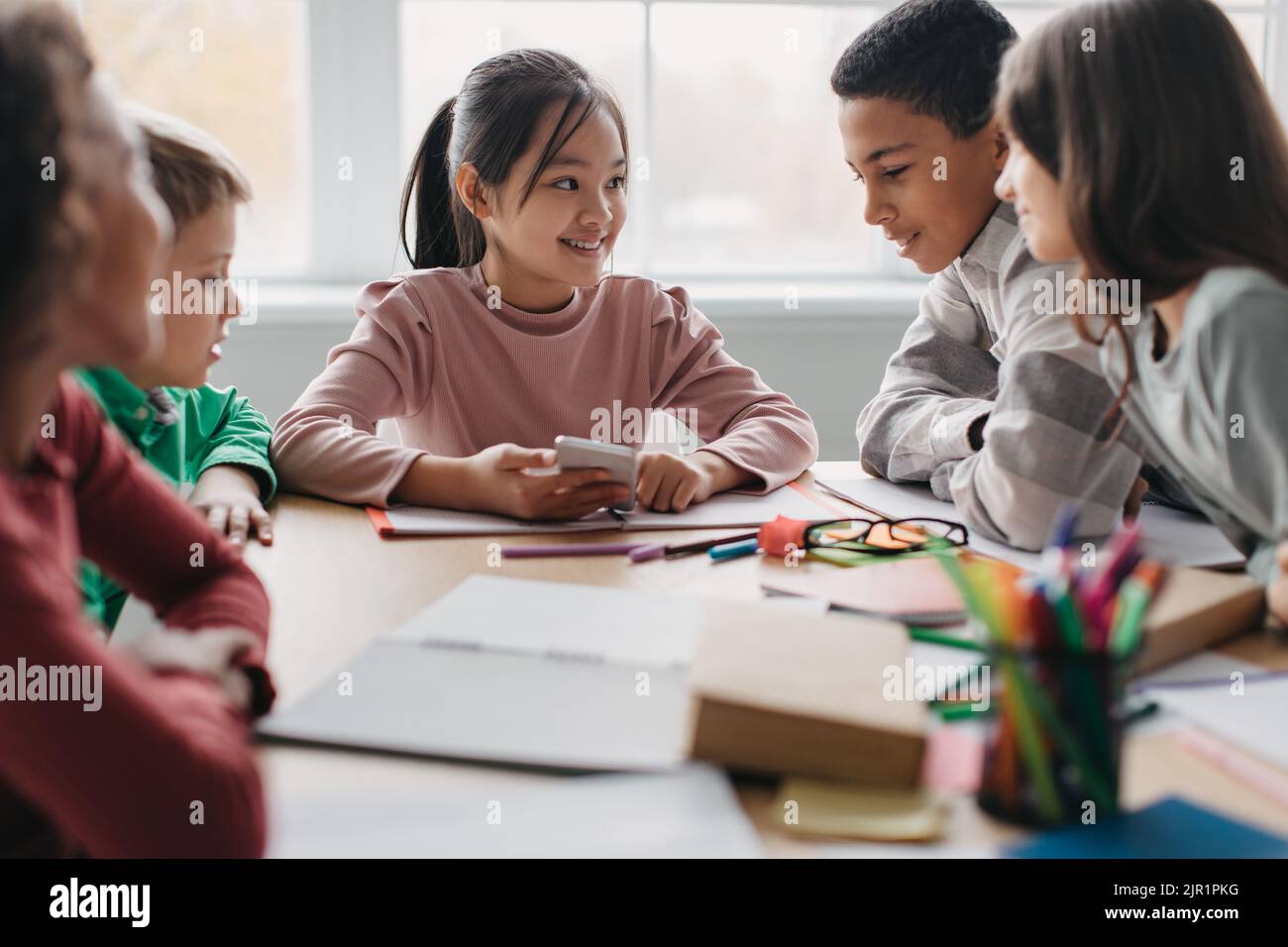 Glückliche Multikulturelle Schulkinder, Die Während Der Pause Im Klassenzimmer Das Telefon Benutzen Stockfoto