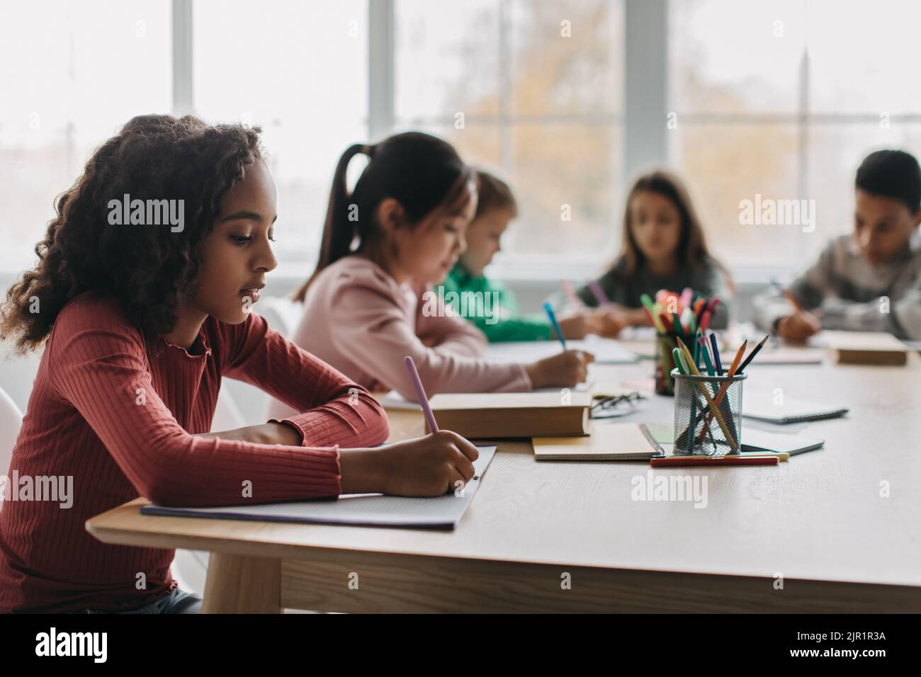 African Schoolgirl Nimmt Notizen Sitzen Mit Verschiedenen Klassenkameraden Im Klassenzimmer Stockfoto