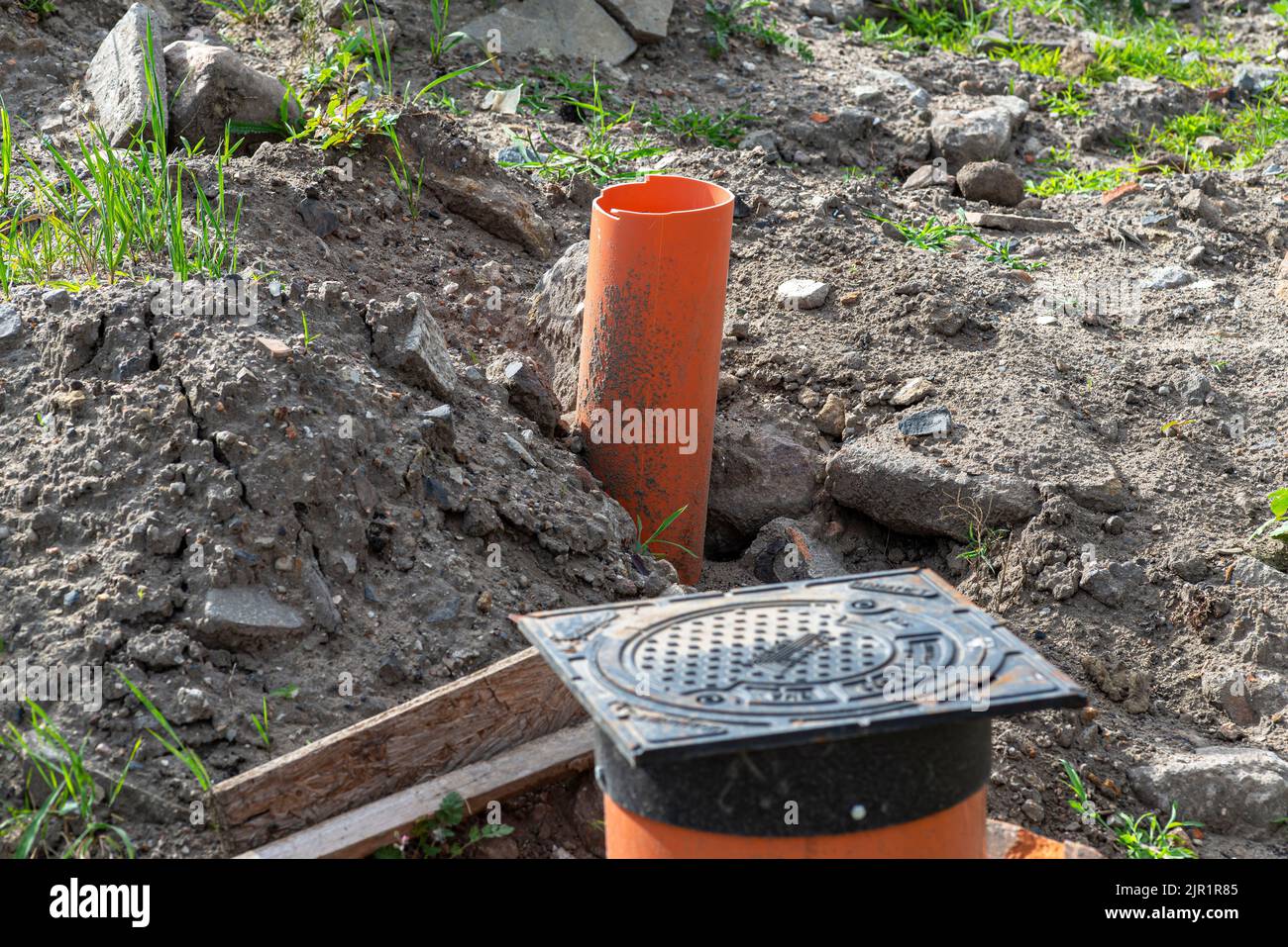 Inspektion der Abwasseranlage mit einem geschlossenen gusseisernen Schachtloch, sichtbaren Kunststoffrohren. Stockfoto