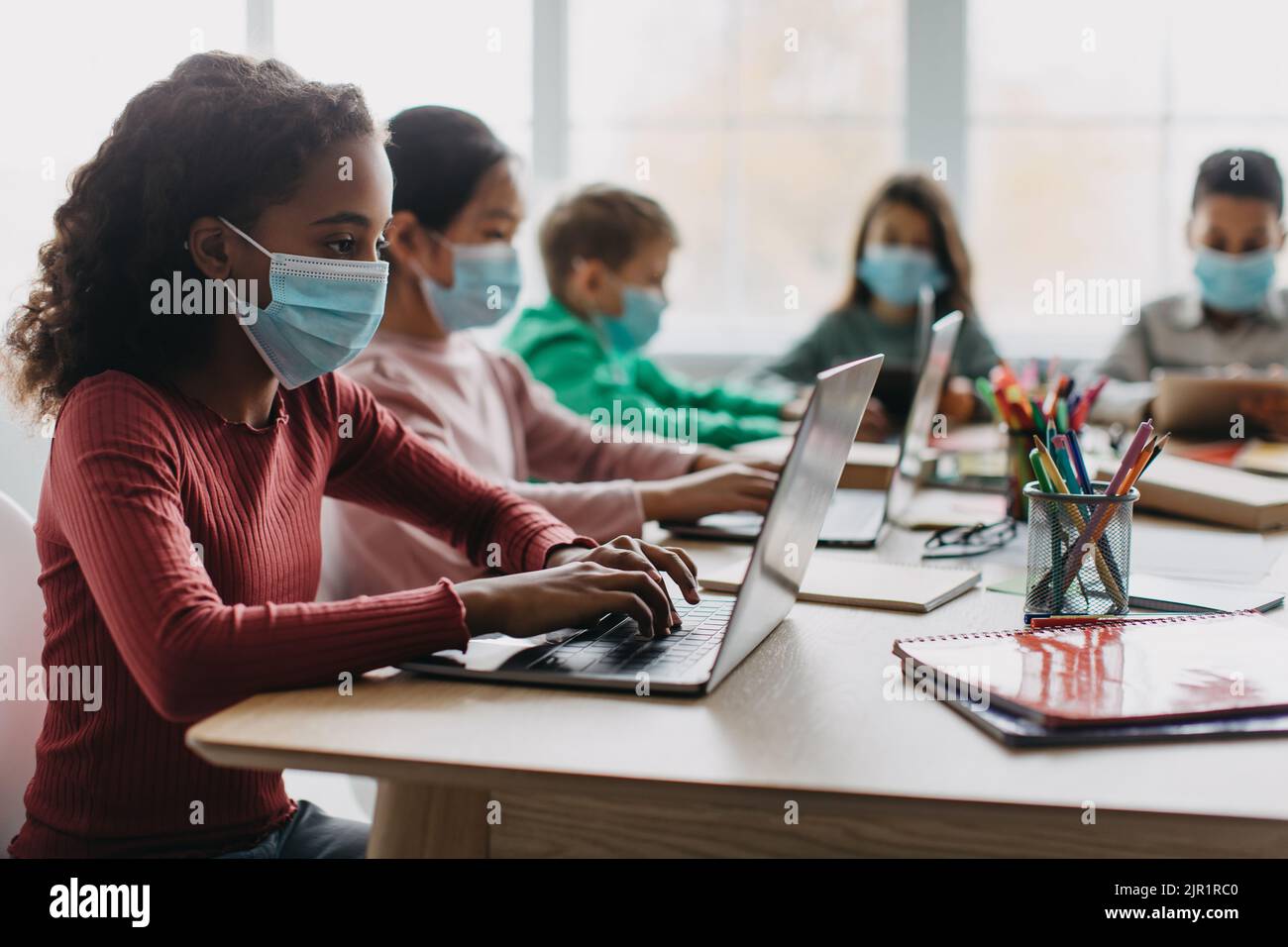 Verschiedene Schulkinder, Die Im Klassenzimmer Computer Mit Gesichtsmasken Verwenden Stockfoto