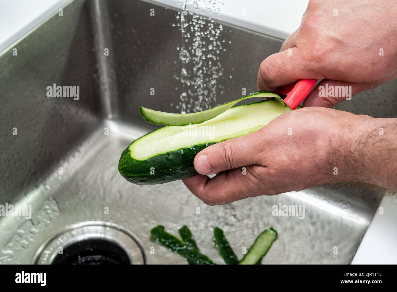 Eine Gurke zum Essen über dem Waschbecken schälen Stockfoto