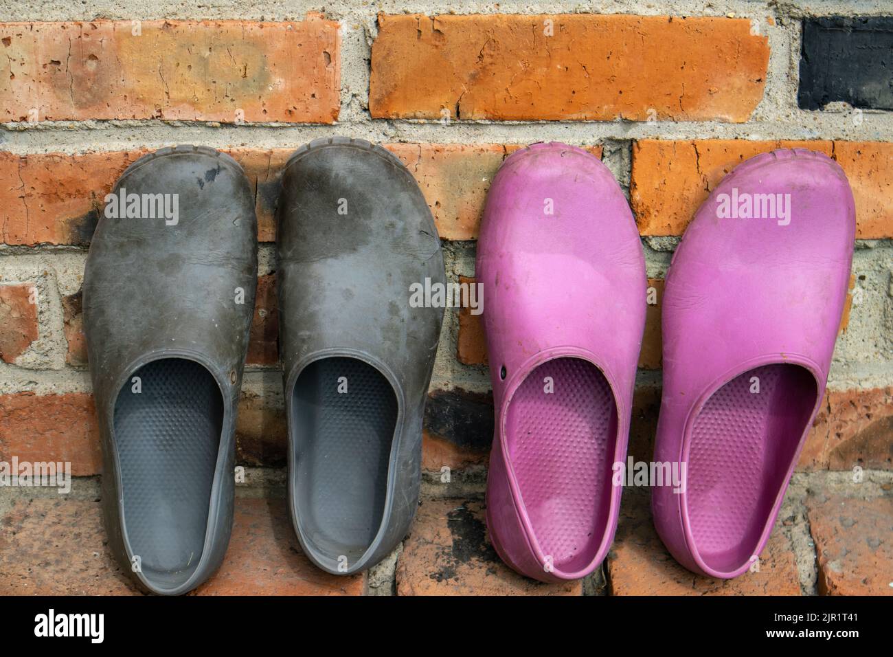 Zwei Paar Gummi-Galoschen in Schwarz und Pink auf dem Hintergrund einer alten Ziegelwand Stockfoto