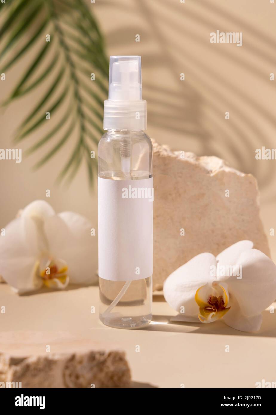 Sprühen Sie die Dispenser-Flasche in der Nähe von weißen Orchideenblumen und beigen Steinen auf hellbeige Nahaufnahme, die Handfläche hinterlässt harte Schatten, Nachbildung. Hautpflegeprodukt p Stockfoto