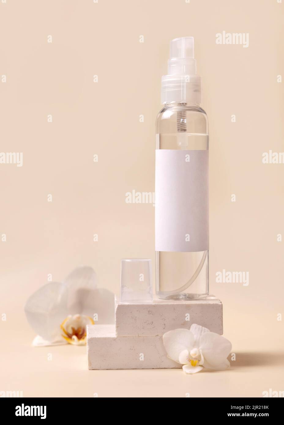 Sprühen Sie die Dispenser-Flasche in der Nähe von weißen Orchideenblumen und beigen Steinen auf hellbeige Nahaufnahme, Mockup. Hautpflege Beauty-Produkt-Paket. Naturkosmetik, Stockfoto