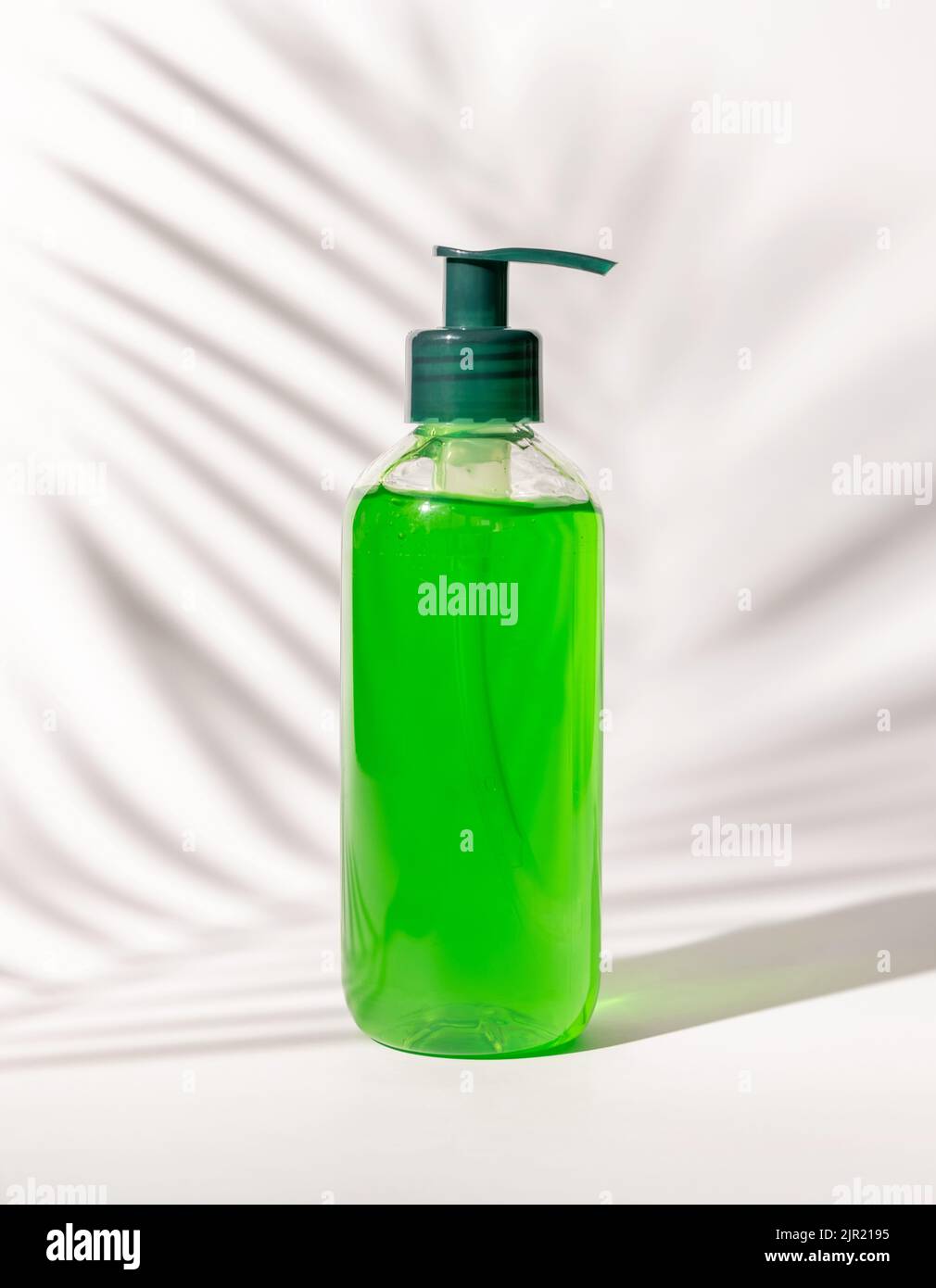 Nachfüllbare Kosmetische Pumpe Spender Flasche mit grüner Flüssigkeit auf weiß gefüllt, Palm Blatt harte Schatten, close up, mockup. Hautpflege Beauty-Produkt, Gesichtsbehandlung Stockfoto