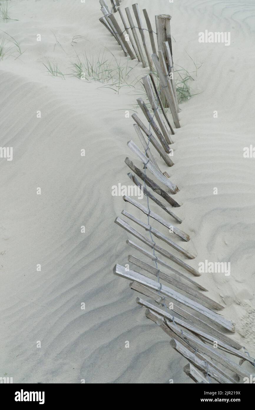 West Wittering, Großbritannien, 21. August 2022: Sand stapelt sich am Fuße der Sanddünen von West Wittering und überwältigt einen alten Holzzaun. Neueres Kunststoffgewebe Stockfoto
