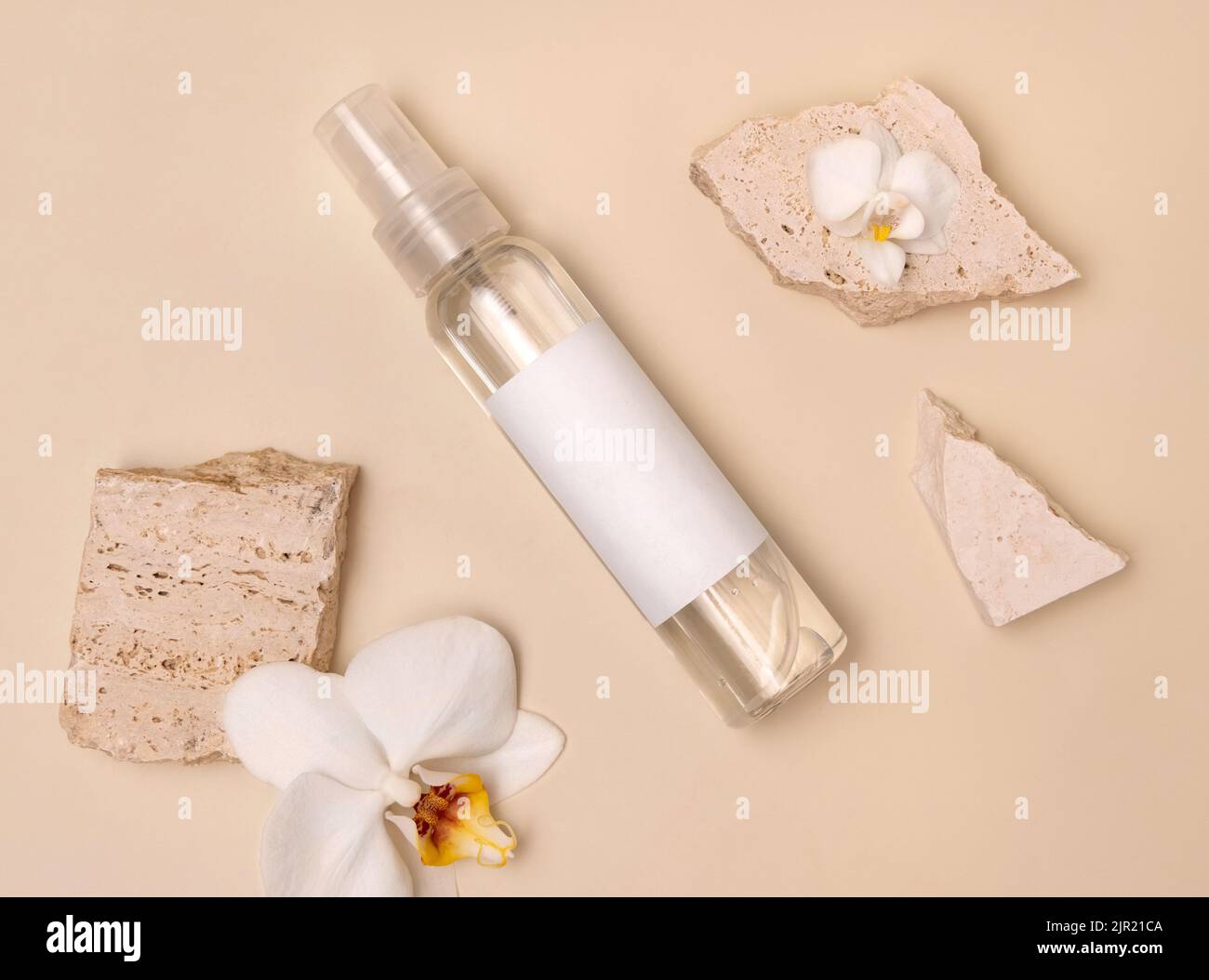 Sprühen Sie die Dispenser-Flasche in der Nähe von weißen Orchideenblumen und beigen Steinen auf hellbeige Draufsicht, Mockup. Hautpflege Beauty-Produkt-Paket. Naturkosmetik, Stockfoto