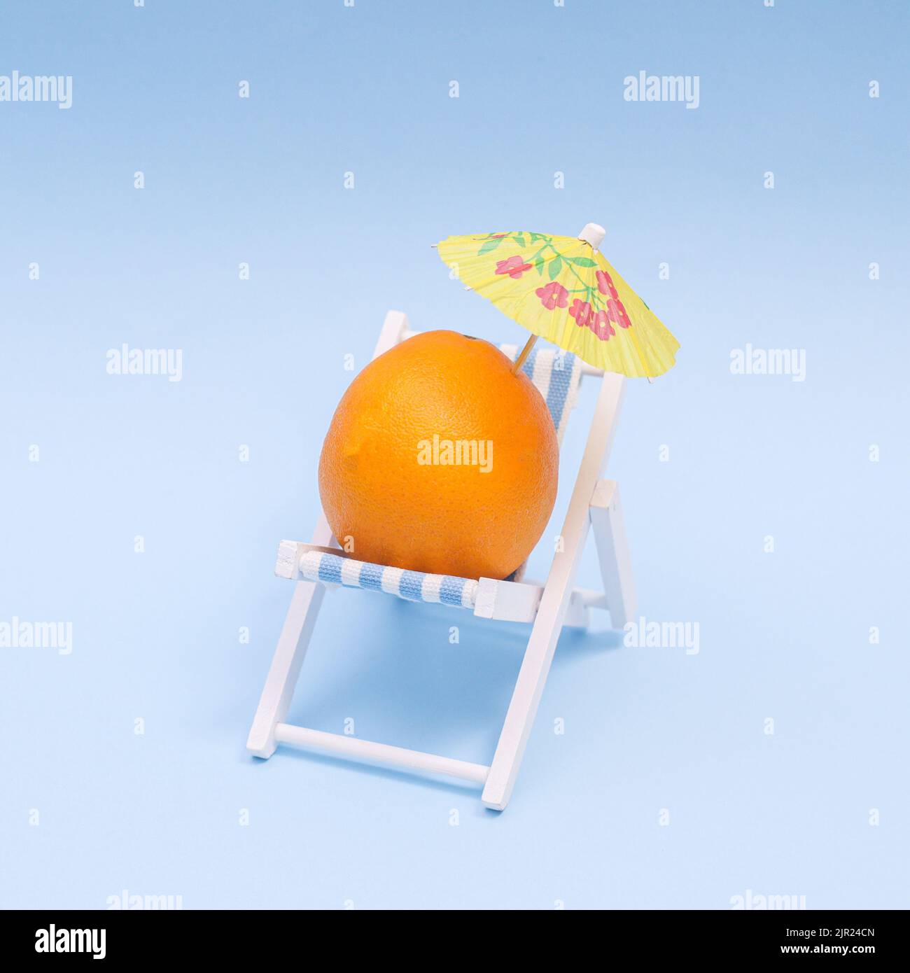 Sommer-Konzept mit orange mit Sonnenschirm auf Strandstuhl auf blauem Hintergrund. Kreatives Konzept Stockfoto