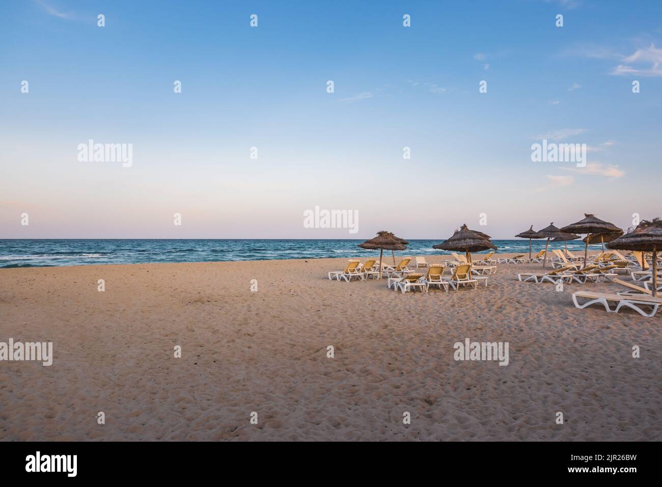 Eine schöne Küste mit Strandliegen und strohgedeckten Vordächern in Djerba, Tunesien Stockfoto