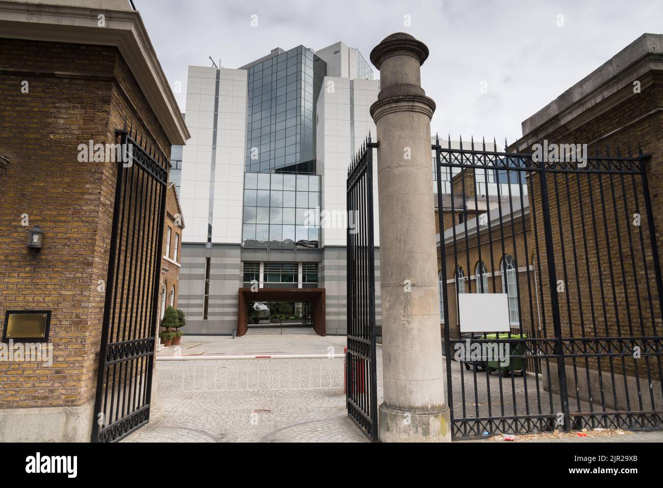 Blick durch ein altes gemauertes, offenes schmiedeeisernes Tor eines alten Hauses zu einem modernen Bürogebäude mit Spiegelfassade für die Koexistenz von altem und Stockfoto