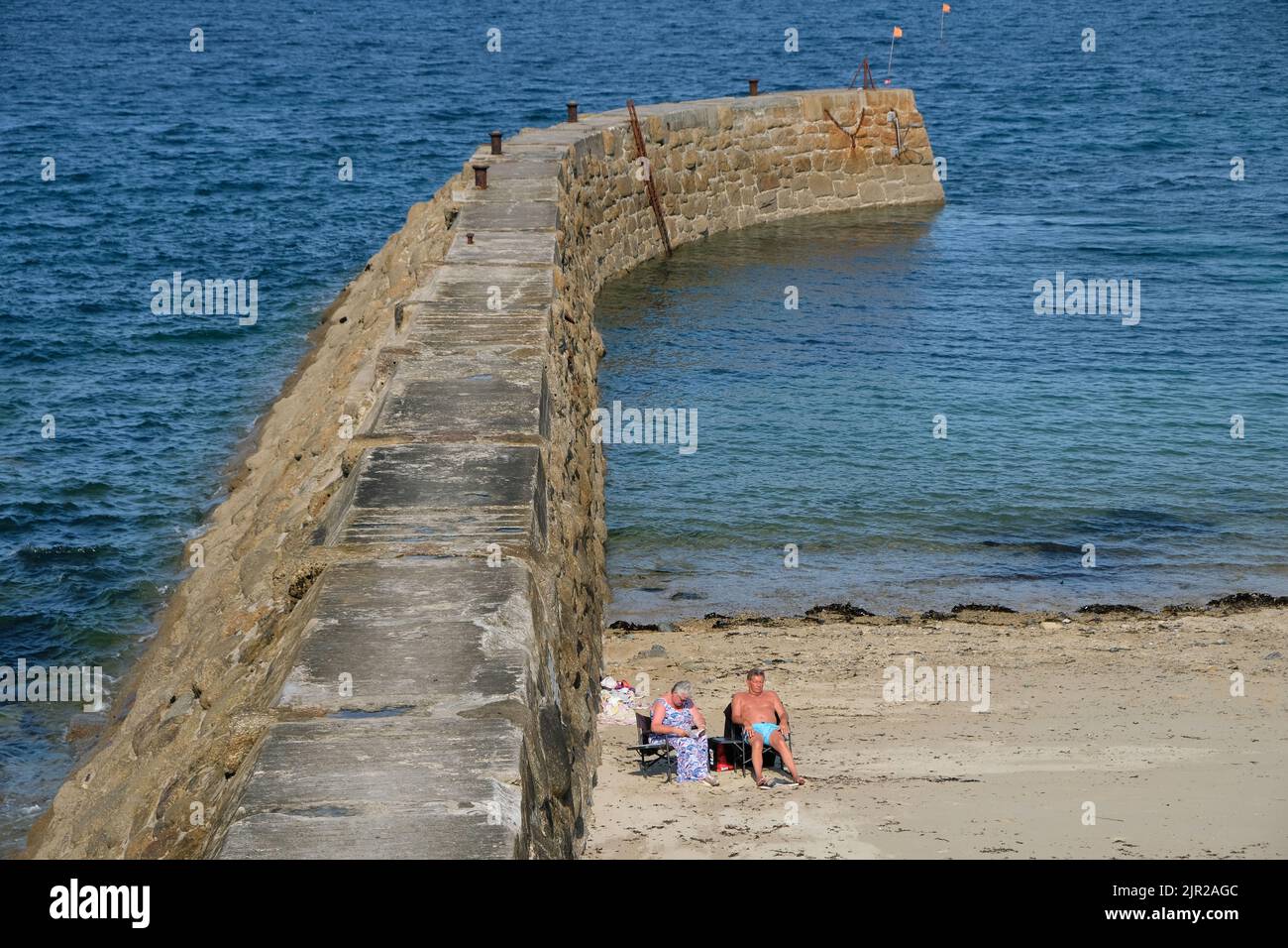 Cornwall, Großbritannien - 2020. September: Ältere kaukasische Paare sonnen sich an einer Hafenmauer an einem Strand in England, Großbritannien Stockfoto