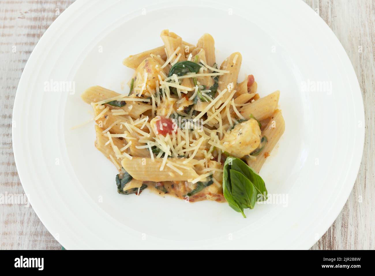 Penne Pasta glutenfreies Abendessen mit Huhn, Käse, Tomatensauce, Basilikum auf weißem Teller von oben Stockfoto