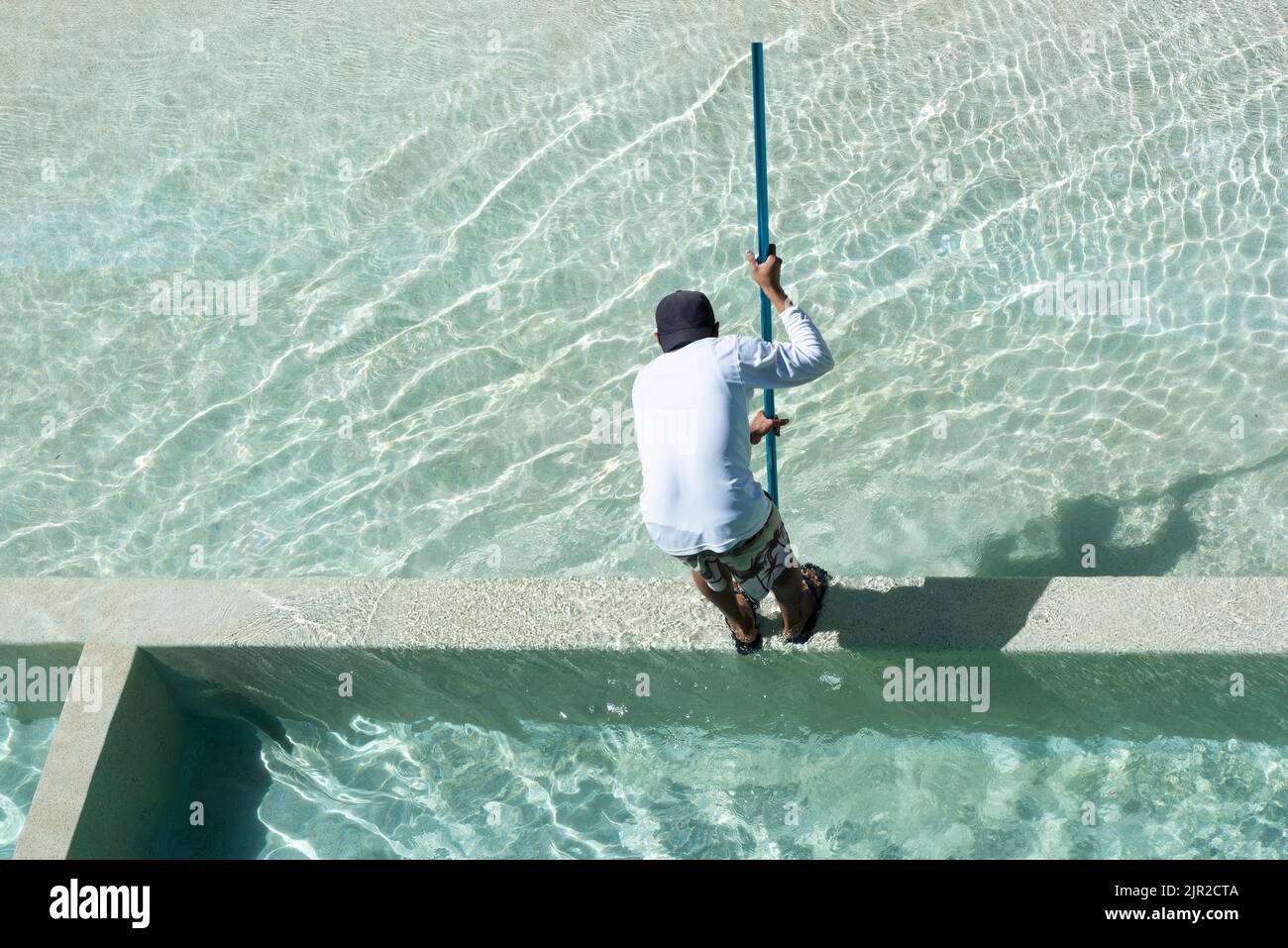 Rückansicht von oben aufgenommen, als ein Wartungsarbeiter in Mexiko einen Pool mit einer Bürste reinigte Stockfoto