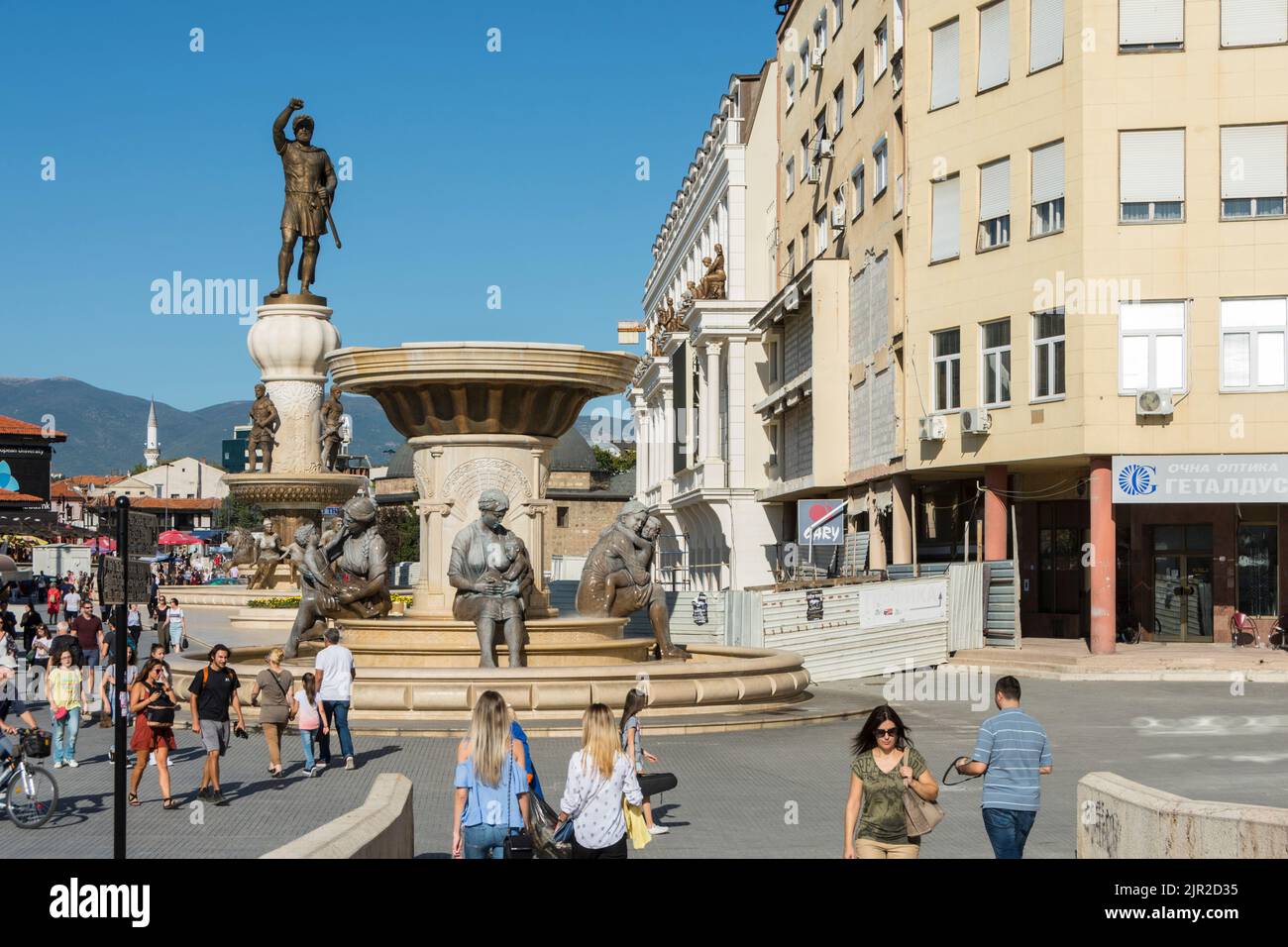 Menschen, die zwischen den vielen Brunnen und Statuen auf dem Karpoš Rebellionsplatz im Zentrum von Skopje, Nordmakedonien, wandern. Stockfoto