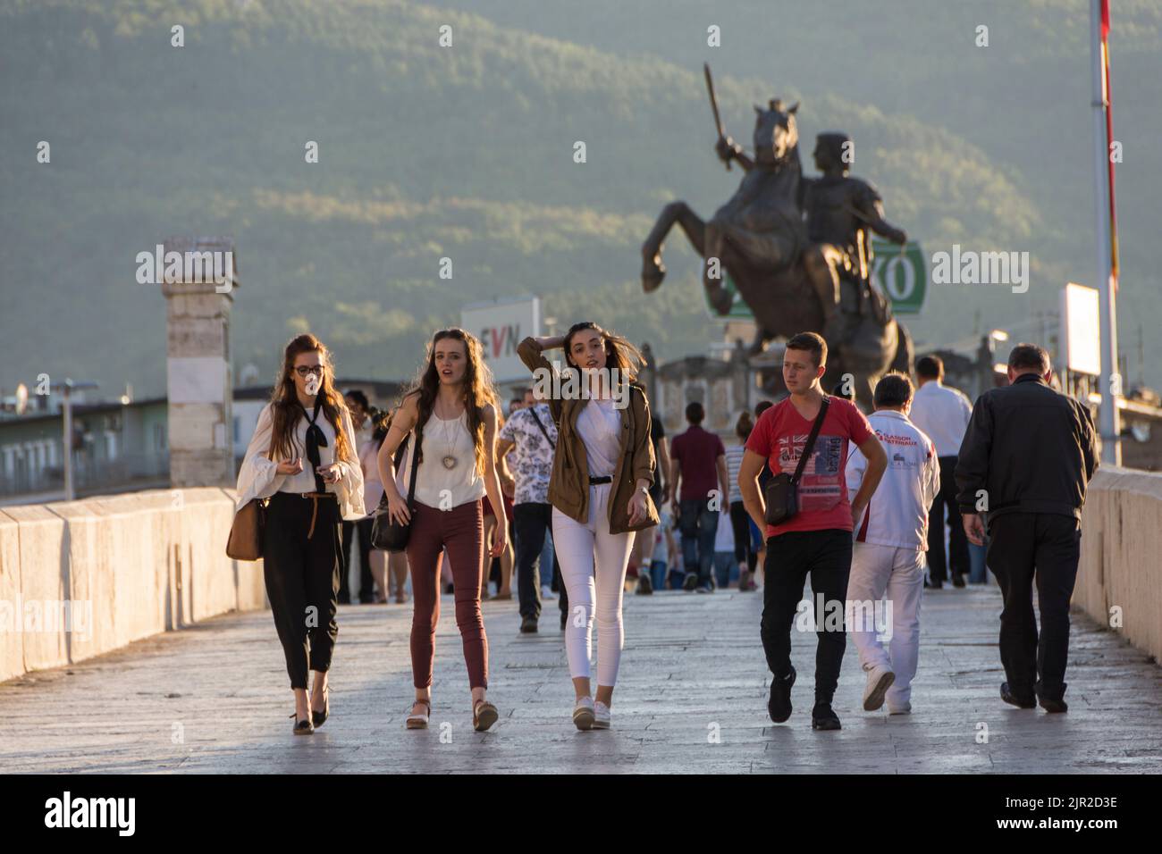 Fröhliche Jugendliche gehen auf der Steinbrücke in Skopje, der Hauptstadt von Nord-Mazedonien. Statue von Alexander dem Großen („Reiterkrieger“) im Hintergrund Stockfoto
