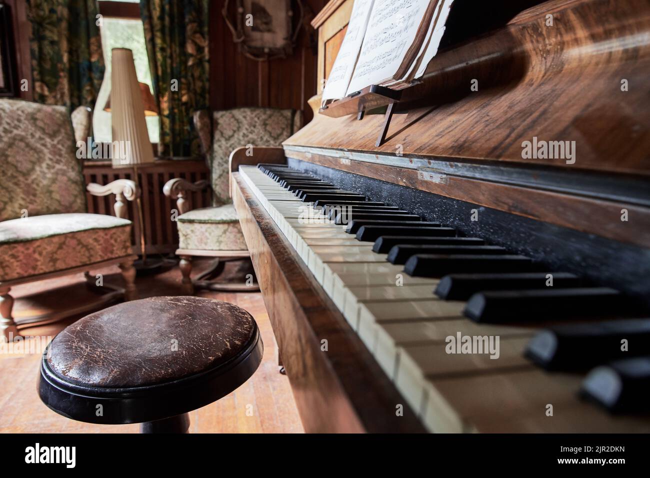 Nahaufnahme eines alten Klaviers mit zwei alten Sesseln dahinter Stockfoto