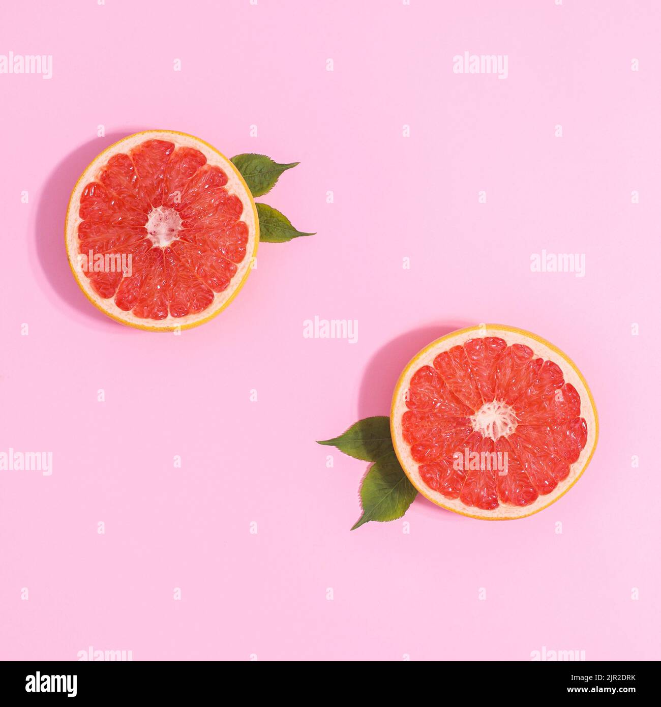 Zwei halbe Stücke Grapefruit mit grünen Blättern auf pastellrosa Hintergrund. Kreative Kopierfläche flach liegend Stockfoto