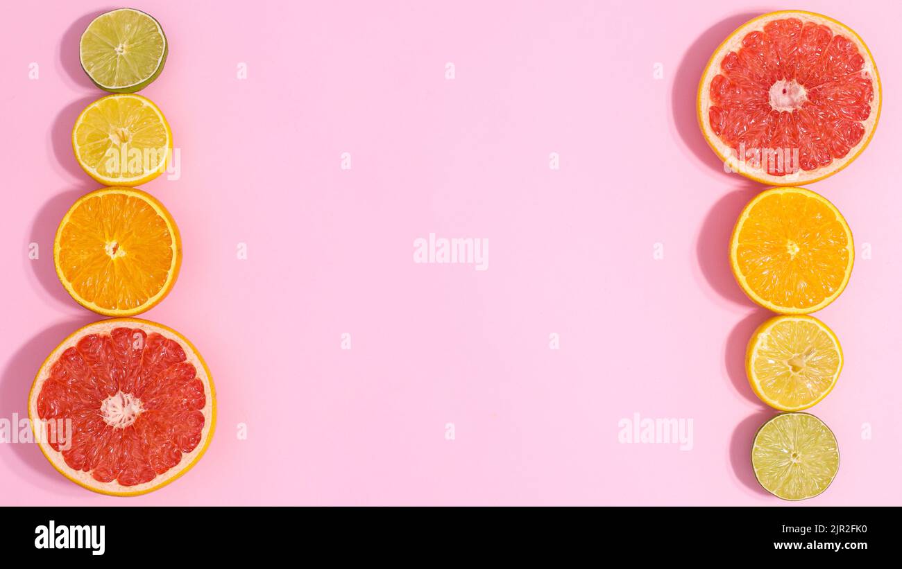 Pastellrosa Hintergrund mit geschnittenen Zitrusfrüchten auf der rechten und linken Seite. Kopierraum flach lat. Sommerkonzept Stockfoto