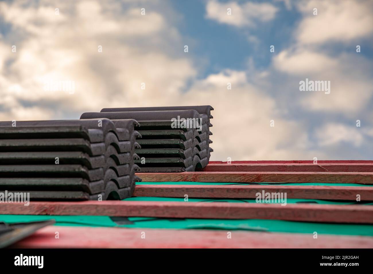 Stapel von Dachziegeln auf einem kahlen Dach mit Wolken dahinter Stockfoto